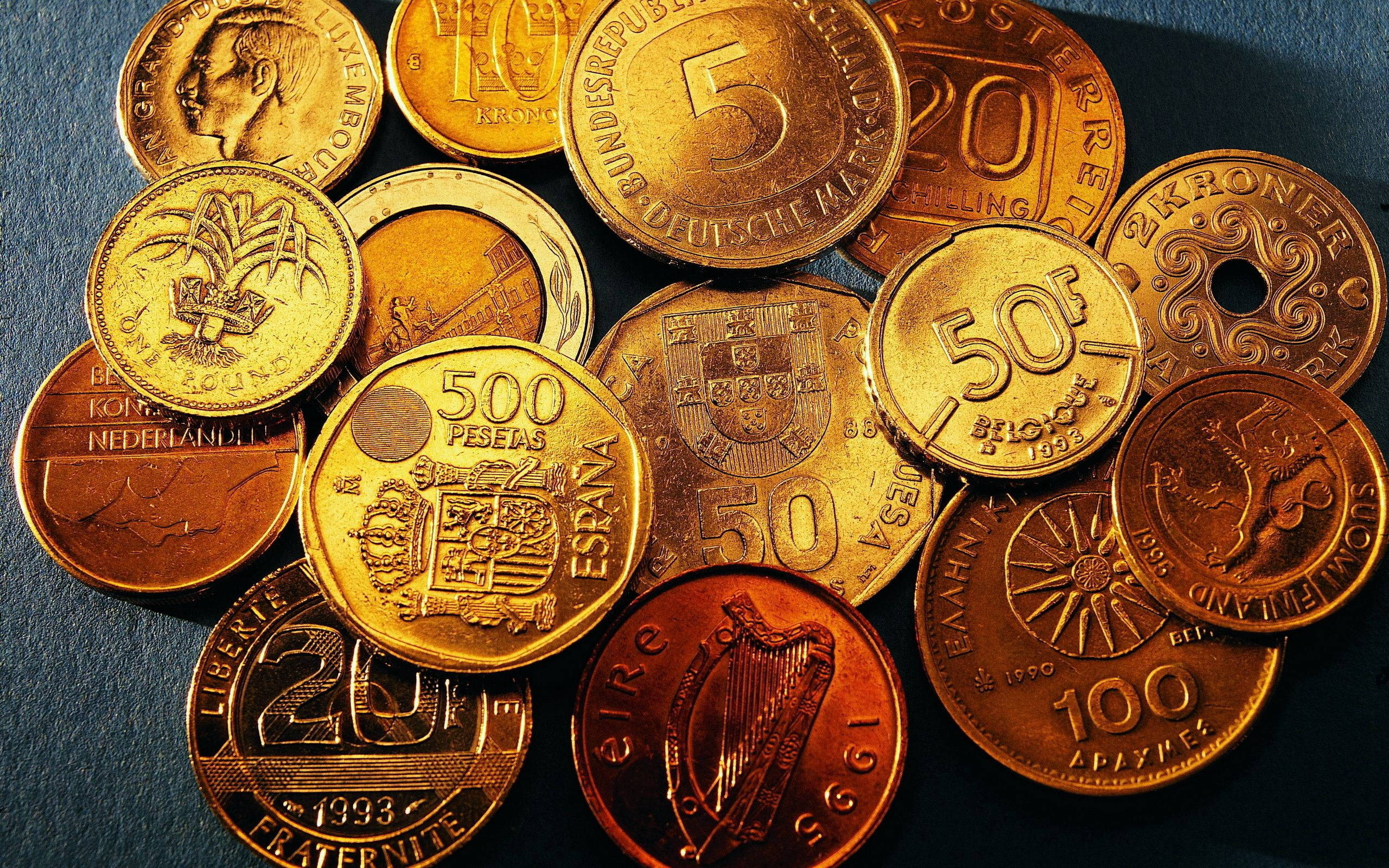 No Money 桌布 壁紙 — 特寫鏡頭：各種國際硬幣以金色和銅色調散落在深藍色表面上。