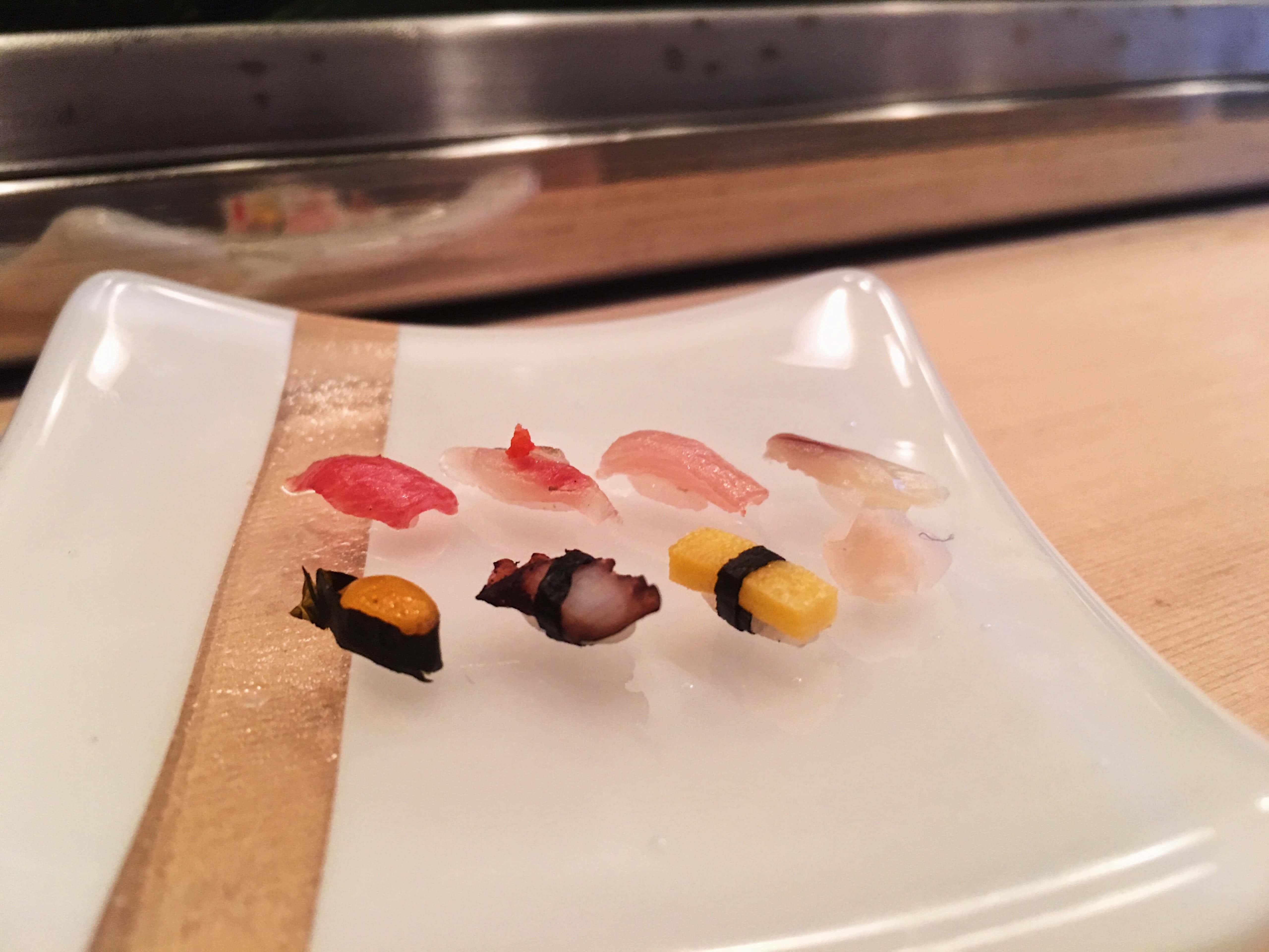 Sushi 桌布 壁紙 — 特寫鏡頭，各種握壽司整齊地排列在帶有木質鑲嵌的白色陶瓷盤上。