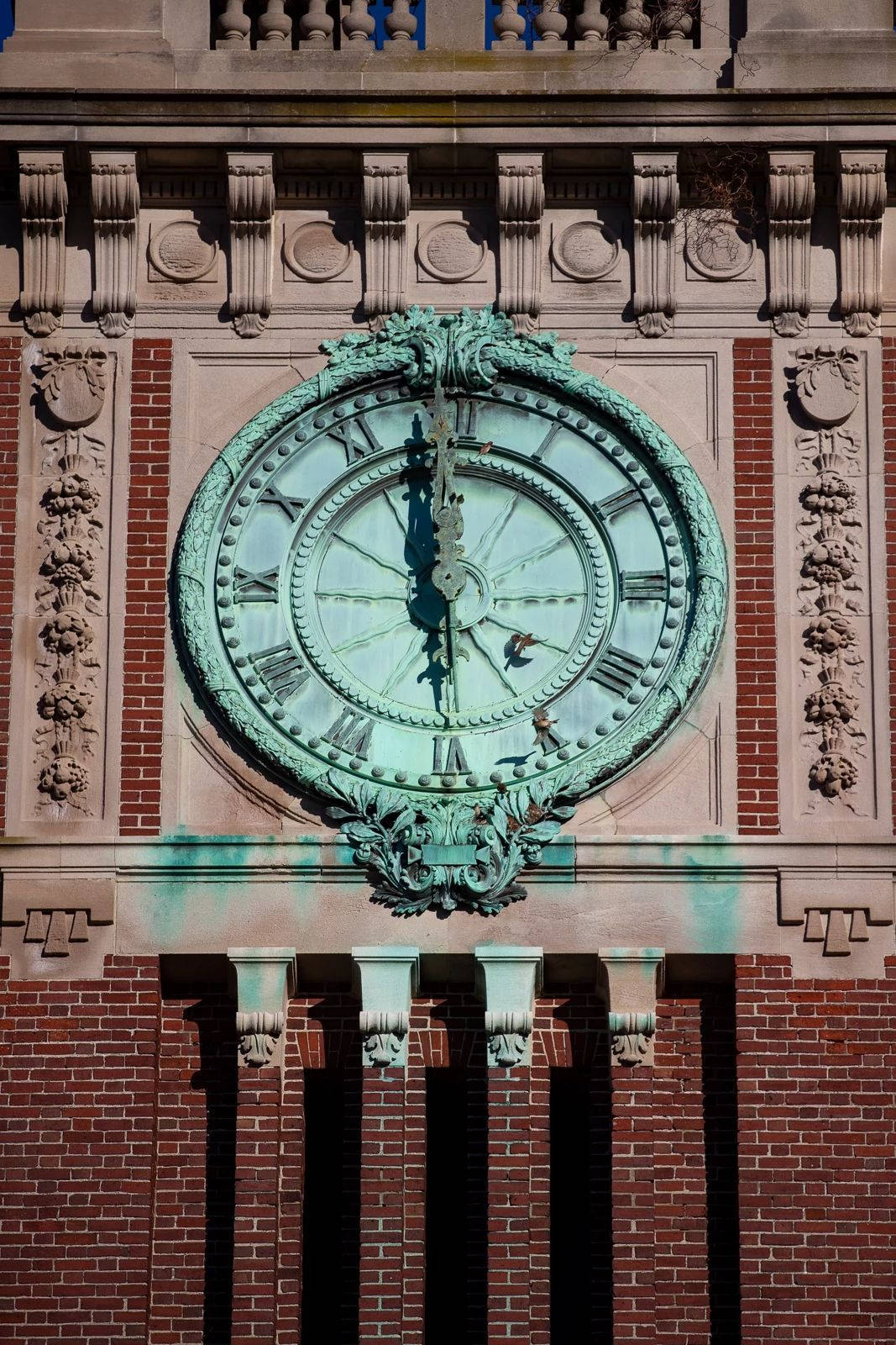 Clock 桌布 壁紙 — 特寫鏡頭：在明亮陽光下，一座紅磚建築外牆上鑲嵌的華麗綠色銅綠時鐘面，帶有羅馬數字。