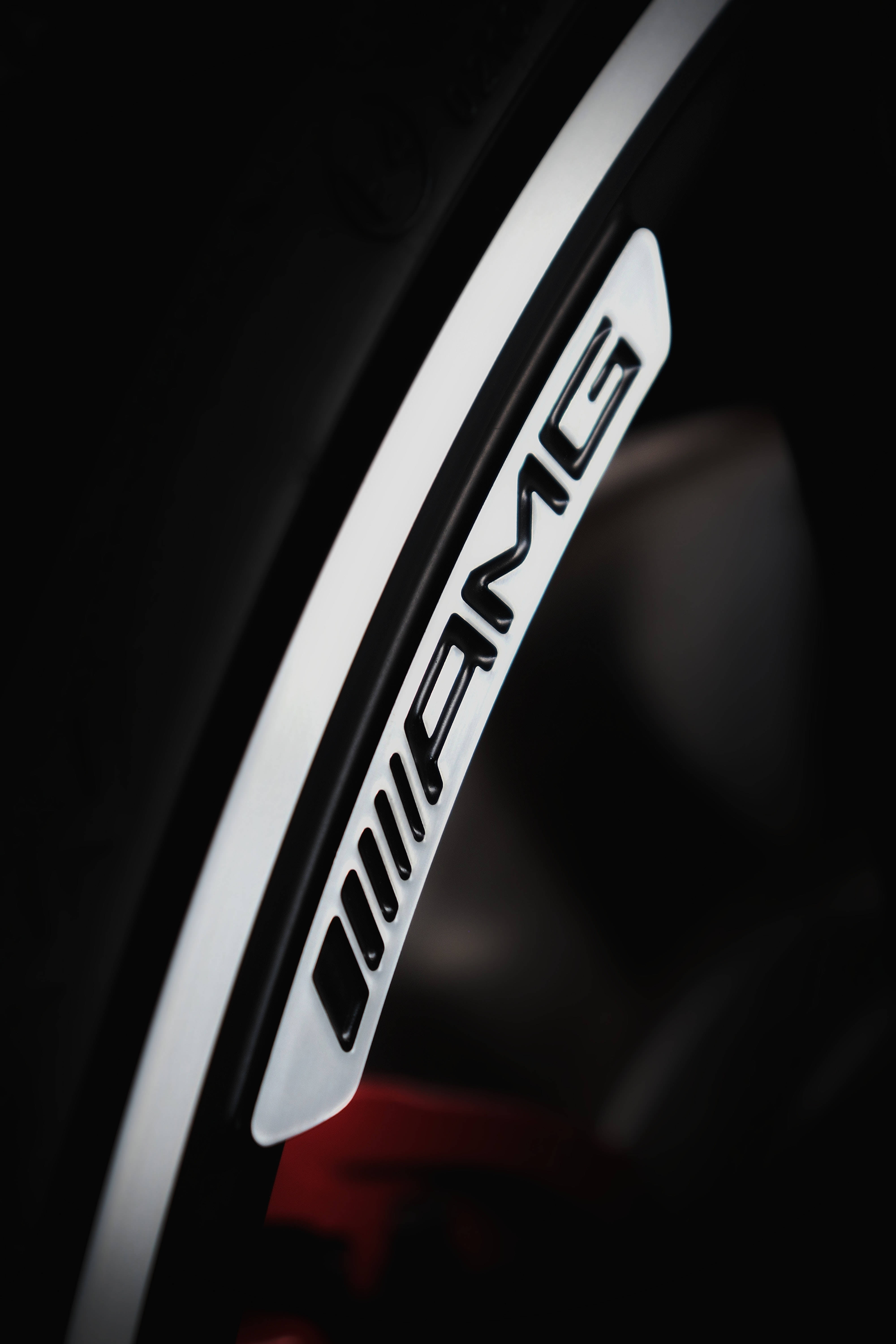 mercedes amg iPhone 桌布 壁紙 — 特寫鏡頭：在深色背景下，汽車輪轂上的AMG標誌線條流暢，光線銳利。