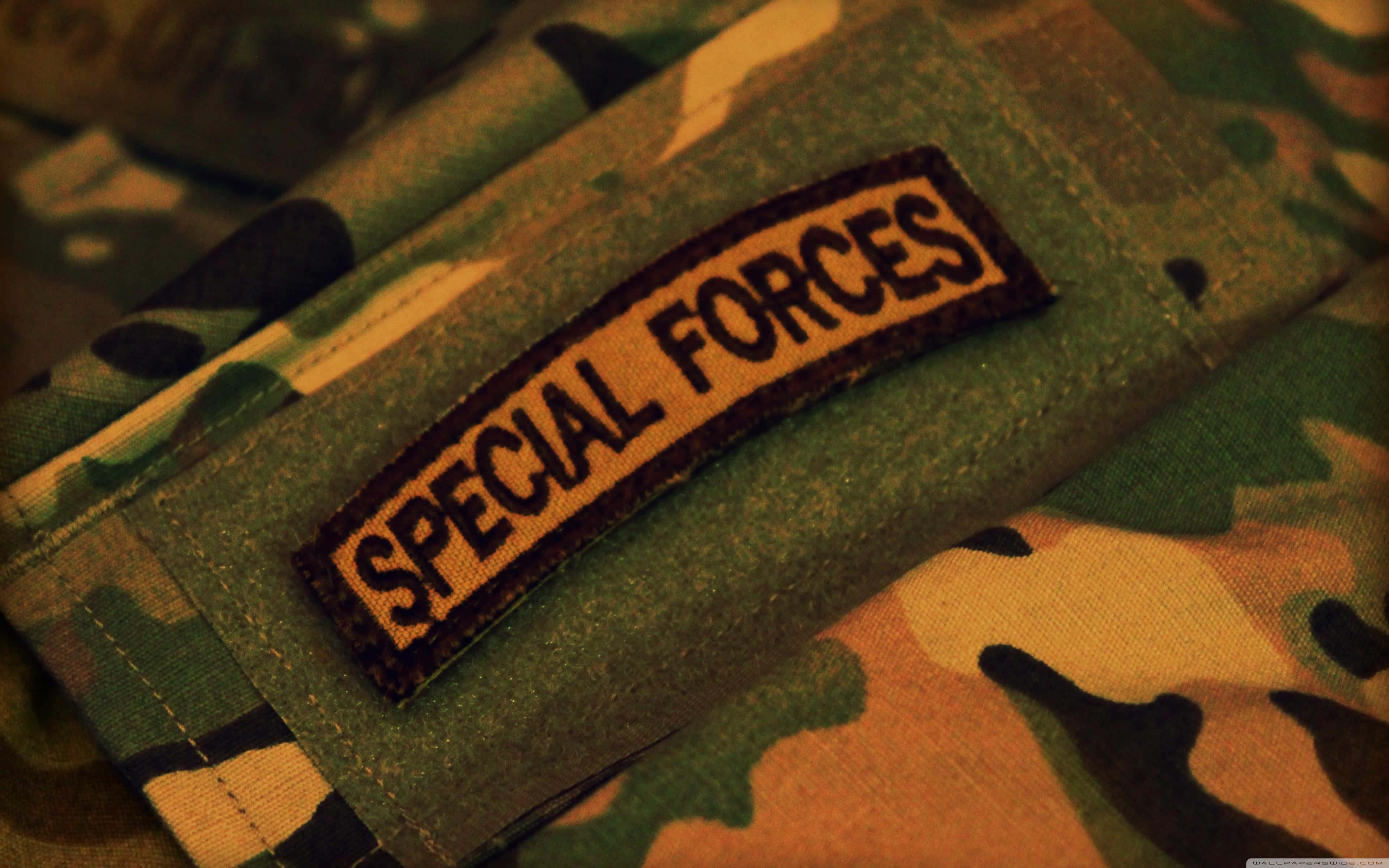 軍隊 桌布 壁紙 — 特寫鏡頭：在溫暖燈光下縫在迷彩軍用裝備上的「SPECIAL FORCES」臂章。