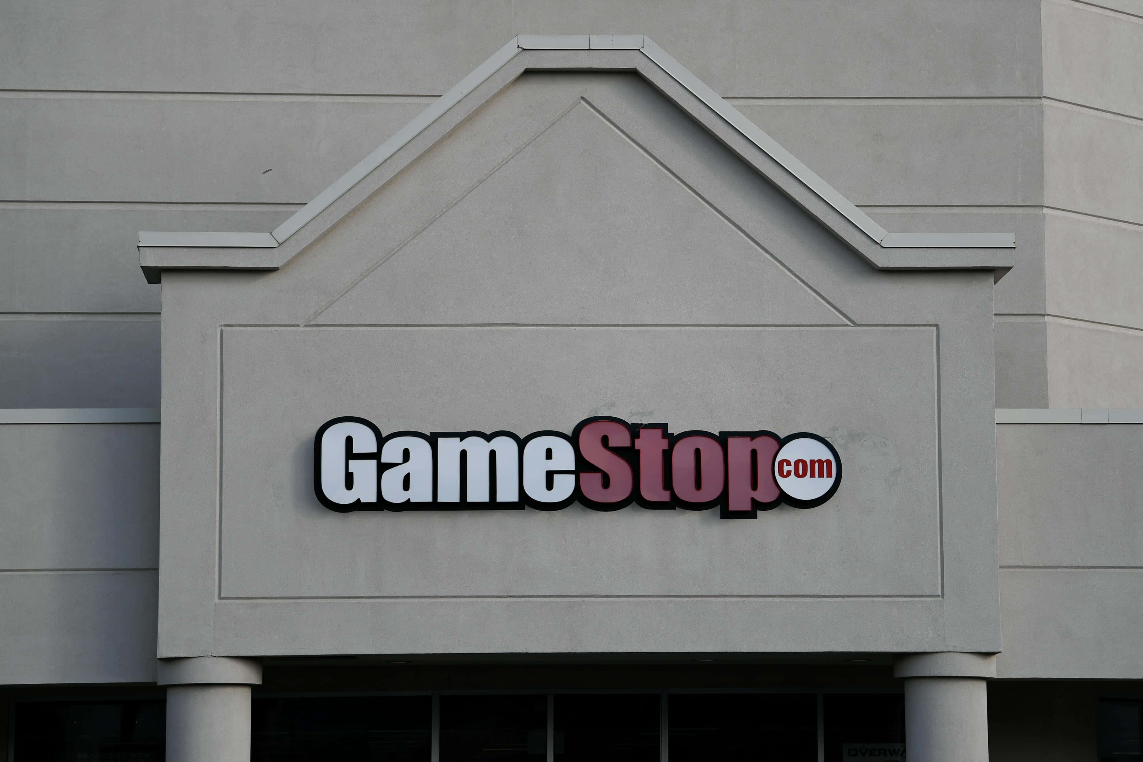 GameStop 桌布 壁紙 — 特寫鏡頭：在陰天之下，安裝在米色商業建築外牆上的GameStop.com商店招牌。