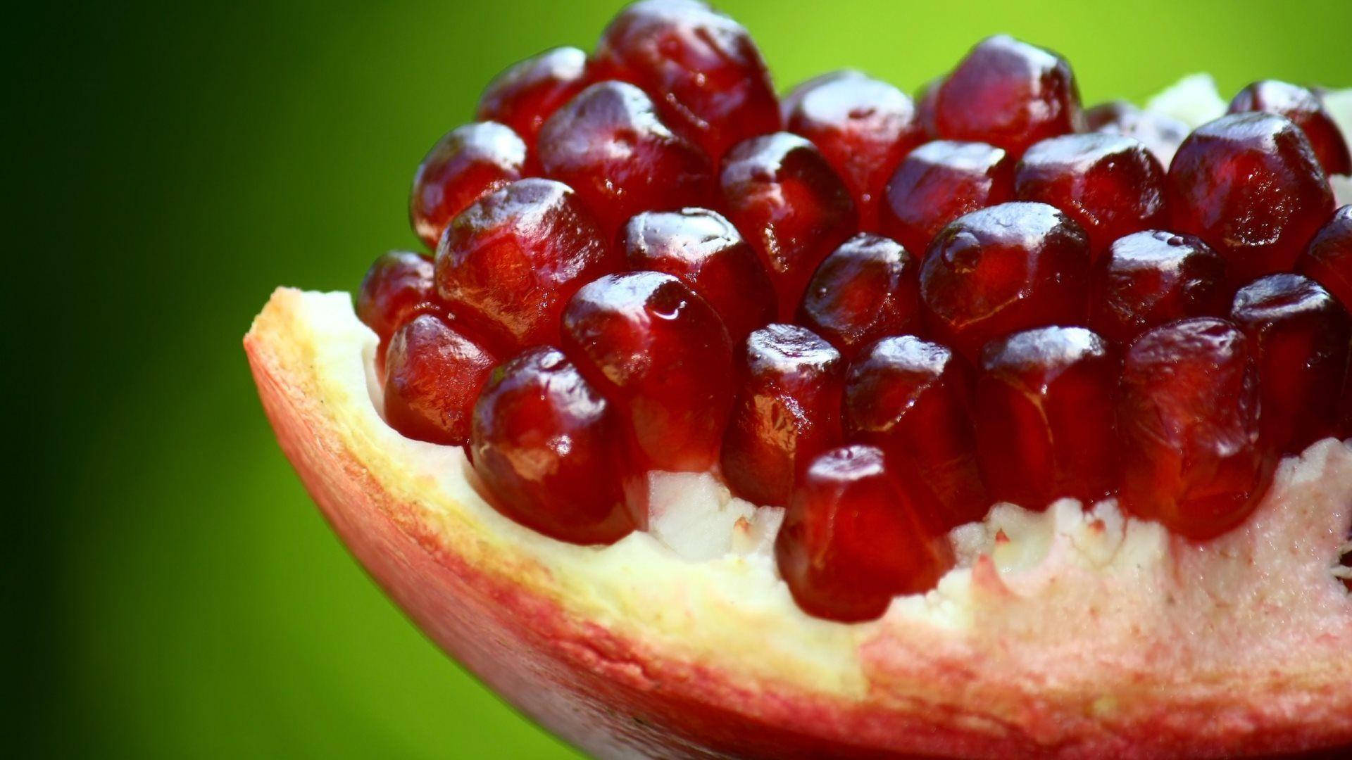 Fruit 桌布 壁紙 — 特寫鏡頭，多汁的紅寶石色石榴籽在柔和的綠色背景上閃閃發光。