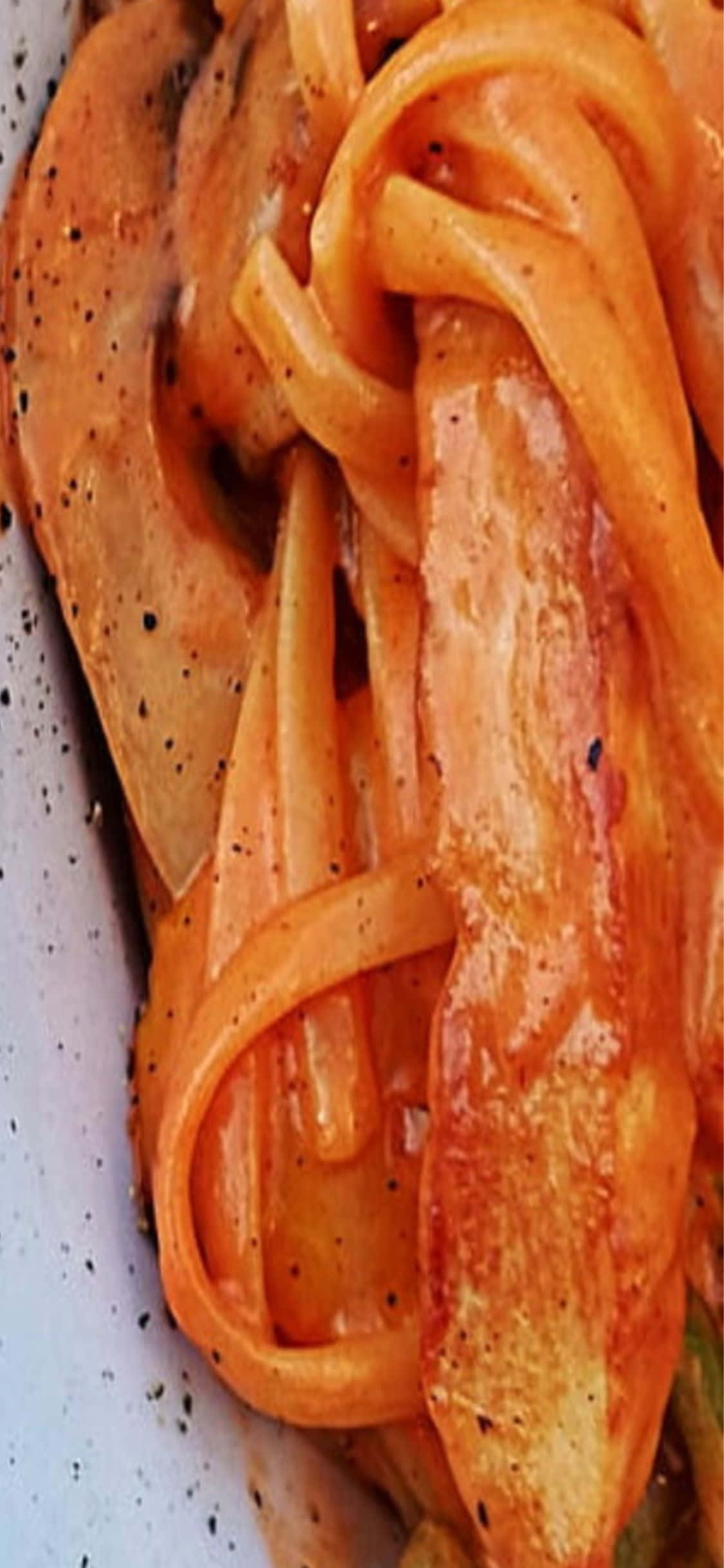 iPhone X Pasta 桌布 壁紙 — 特寫鏡頭：奶油橙色義大利麵搭配切片蘑菇和黑胡椒，放在有斑點的盤子上。