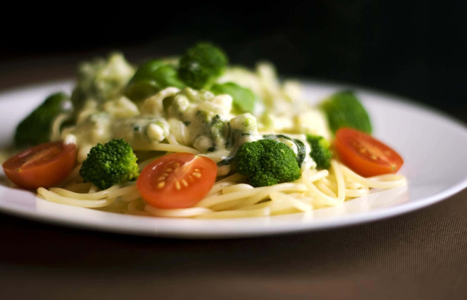 Pasta 桌布 壁紙 — 特寫鏡頭：奶油義大利麵搭配青花菜和櫻桃番茄，放在白色盤子上，背景為深色。