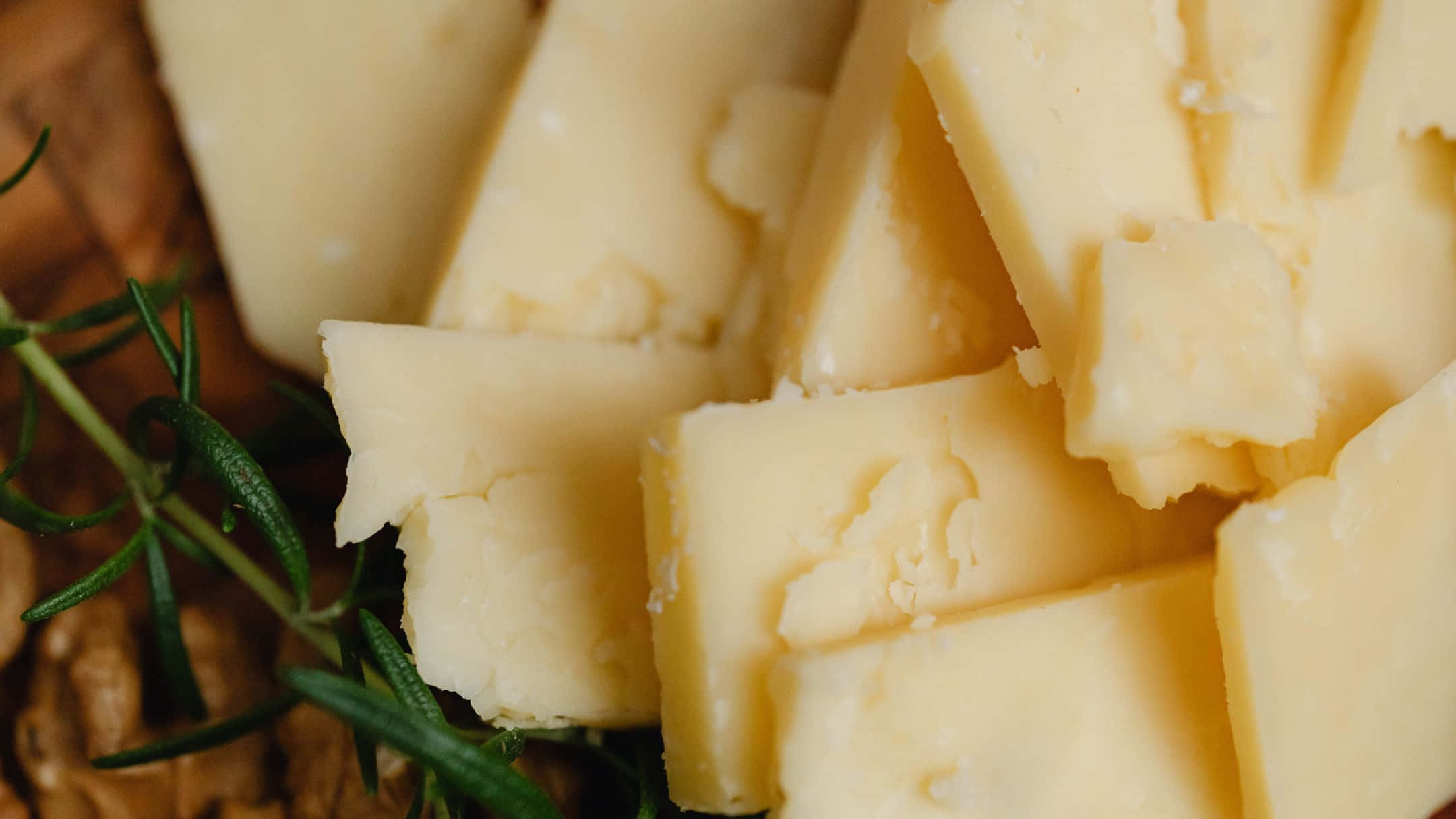 Cheese 桌布 壁紙 — 特寫鏡頭：奶油般淡黃色的起司塊，配上新鮮的綠色迷迭香枝條，置於質樸的木質表面上。