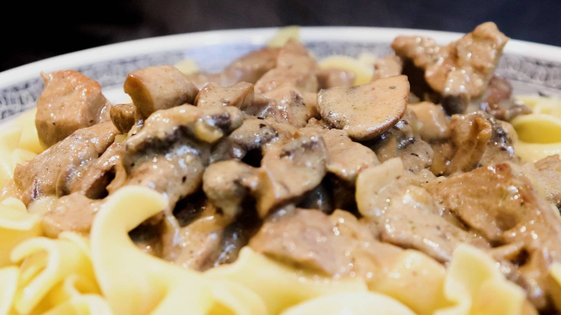 mushrooms 桌布 壁紙 — 特寫鏡頭：奶油蘑菇牛肉斯特羅加諾夫搭配寬蛋麵，盛裝在花紋碗中。