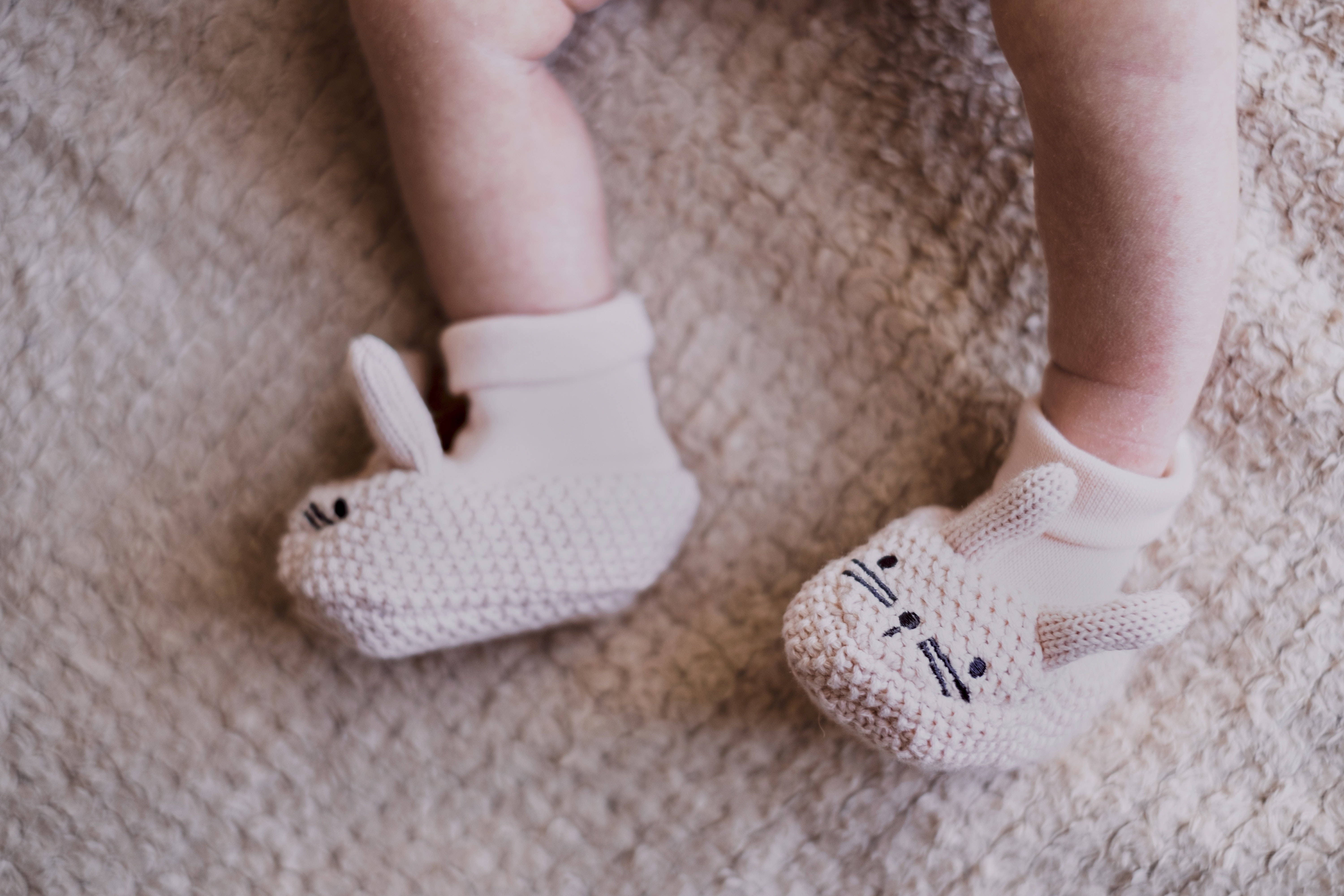 Newborn 桌布 壁紙 — 特寫鏡頭：嬰兒雙腳穿著柔軟米色針織兔兔靴，放在毛絨質感地毯上。