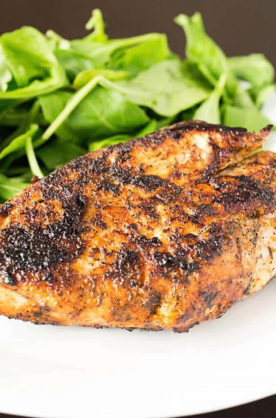 Blackened Chicken 桌布 壁紙 — 特寫鏡頭：完美烤製的雞胸肉，邊緣微焦，搭配新鮮綠色芝麻菜，盛放在白色餐盤上。