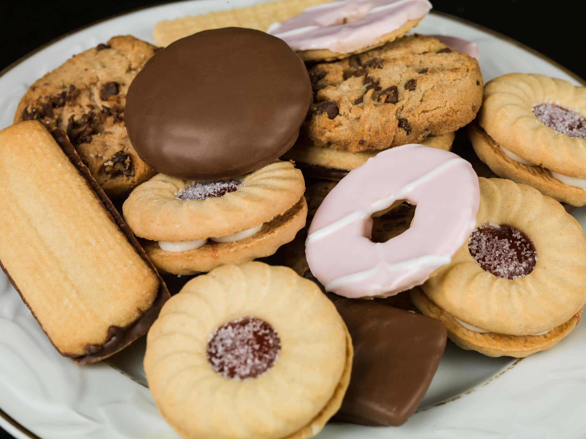 Biscuit 桌布 壁紙 — 特寫鏡頭，展示各種甜點，包括巧克力餅乾和粉紅色糖霜甜甜圈，堆疊在白色盤子上。