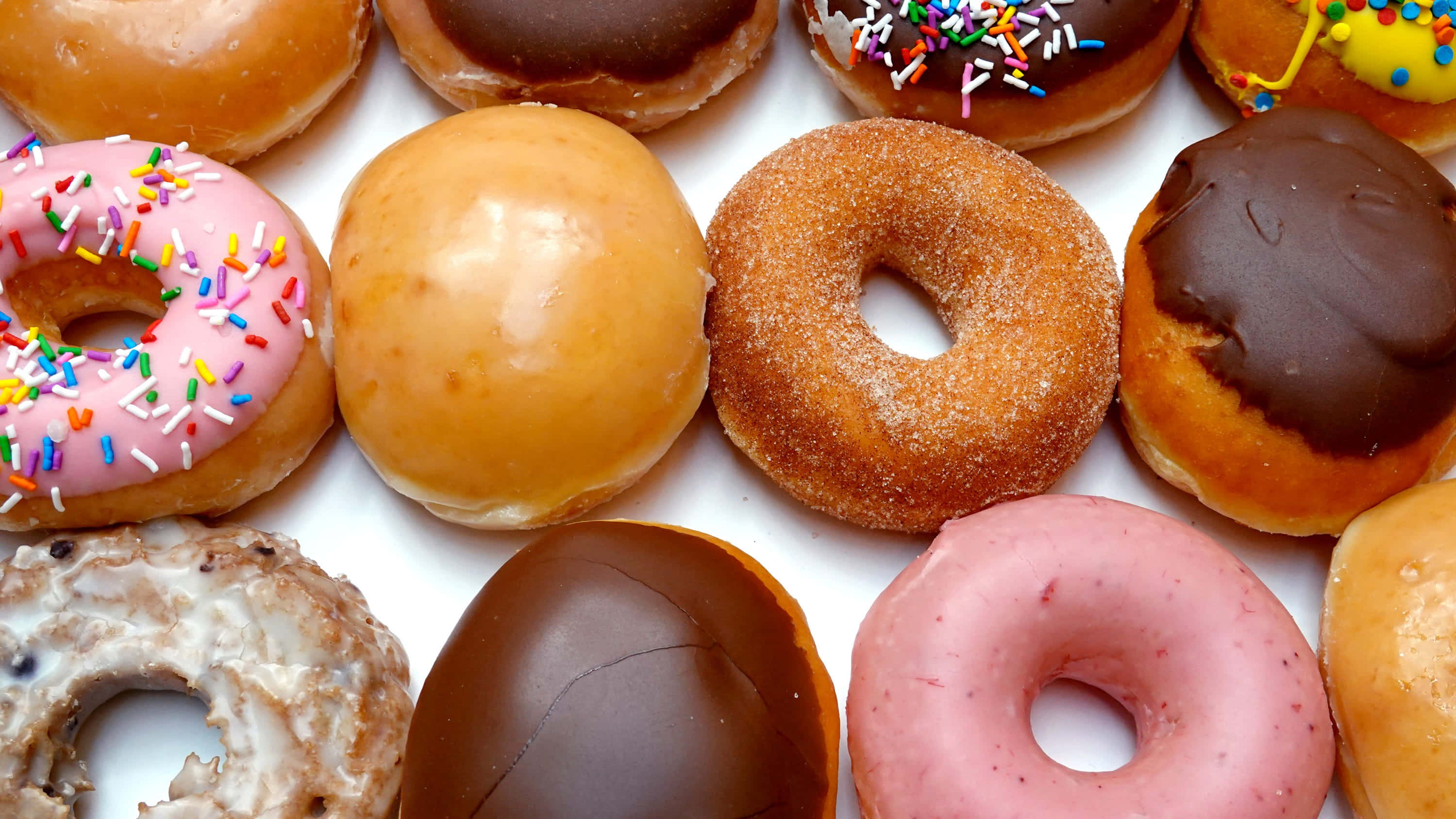 Donut 桌布 壁紙 — 特寫鏡頭，展示各種釉面巧克力碎和粉紅糖霜甜甜圈，排列在白色表面上。