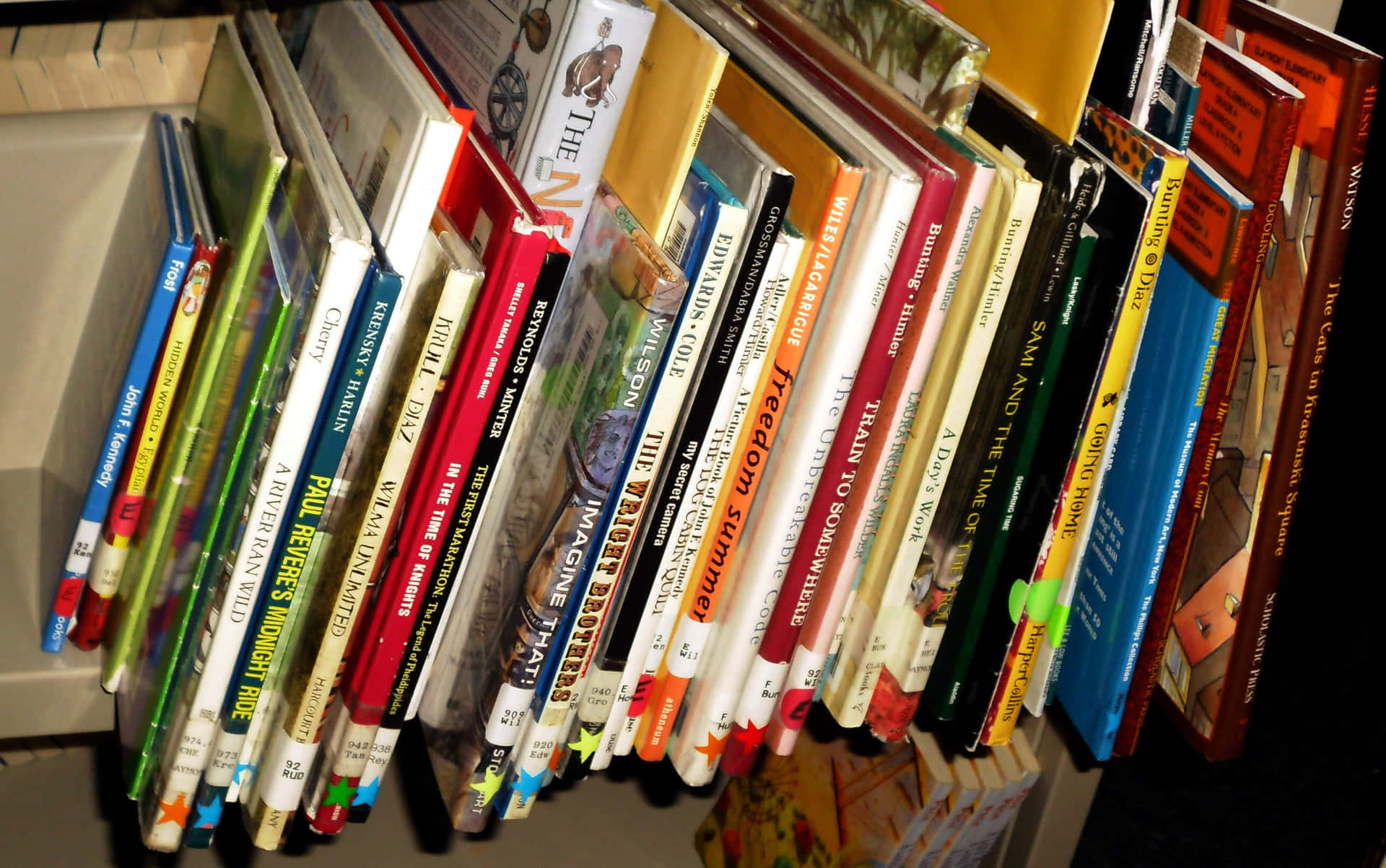 書本 桌布 壁紙 — 特寫鏡頭，展示書架上直立的多彩書籍，書脊和書名清晰可見。