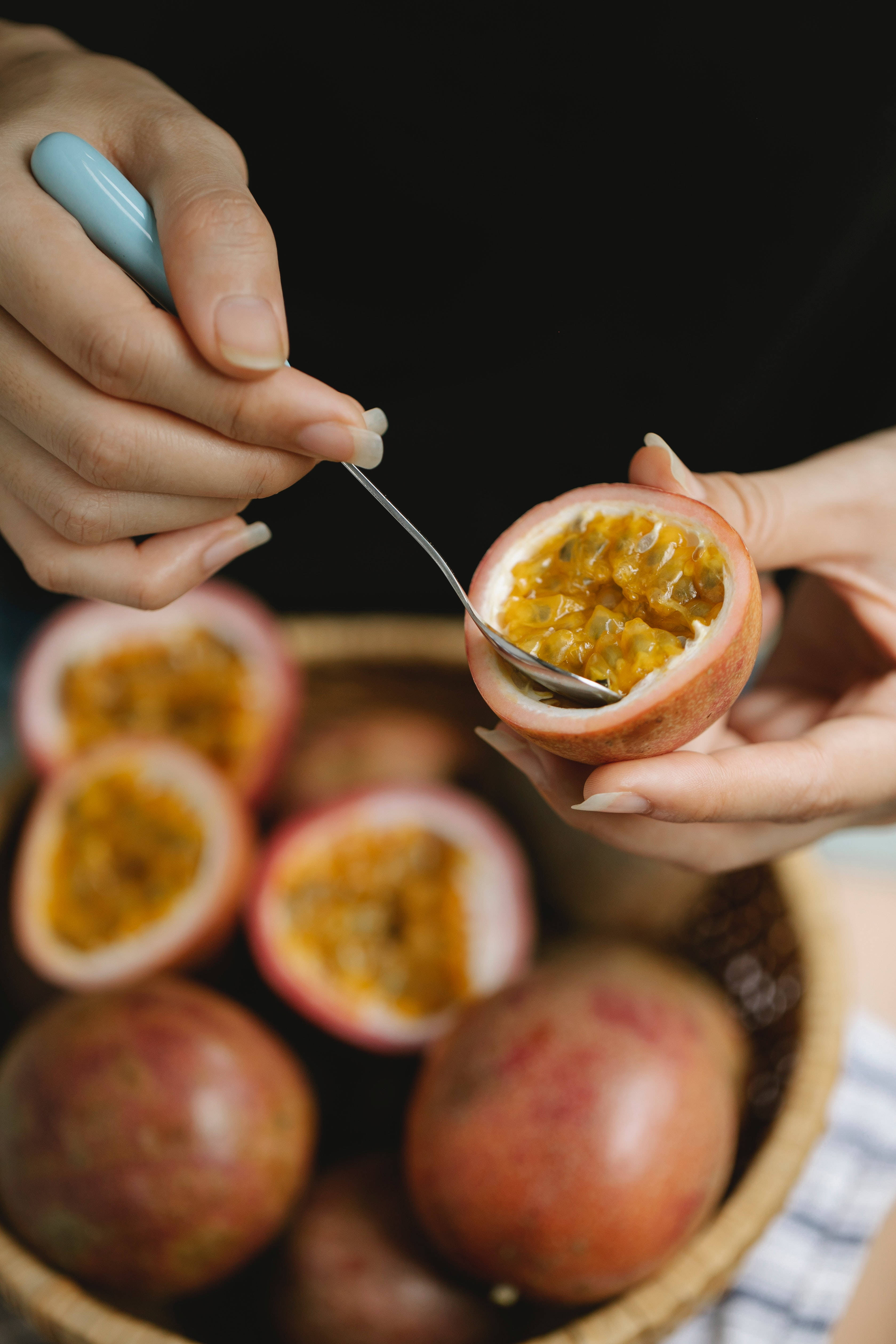 Fruits 桌布 壁紙 — 特寫鏡頭，手用淺藍色手柄從切半的百香果中舀出鮮黃色的果肉。