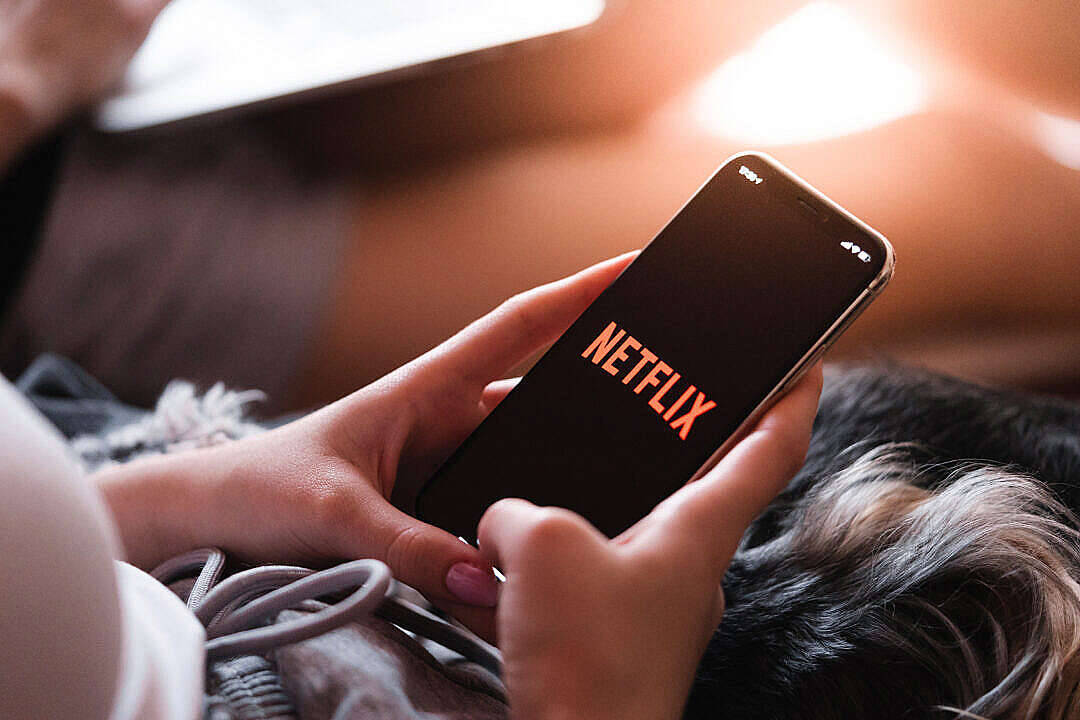 full screen HD 桌布 壁紙 — 特寫鏡頭：手裡拿著一部顯示Netflix標誌的智慧型手機，同時在沙發上休息。