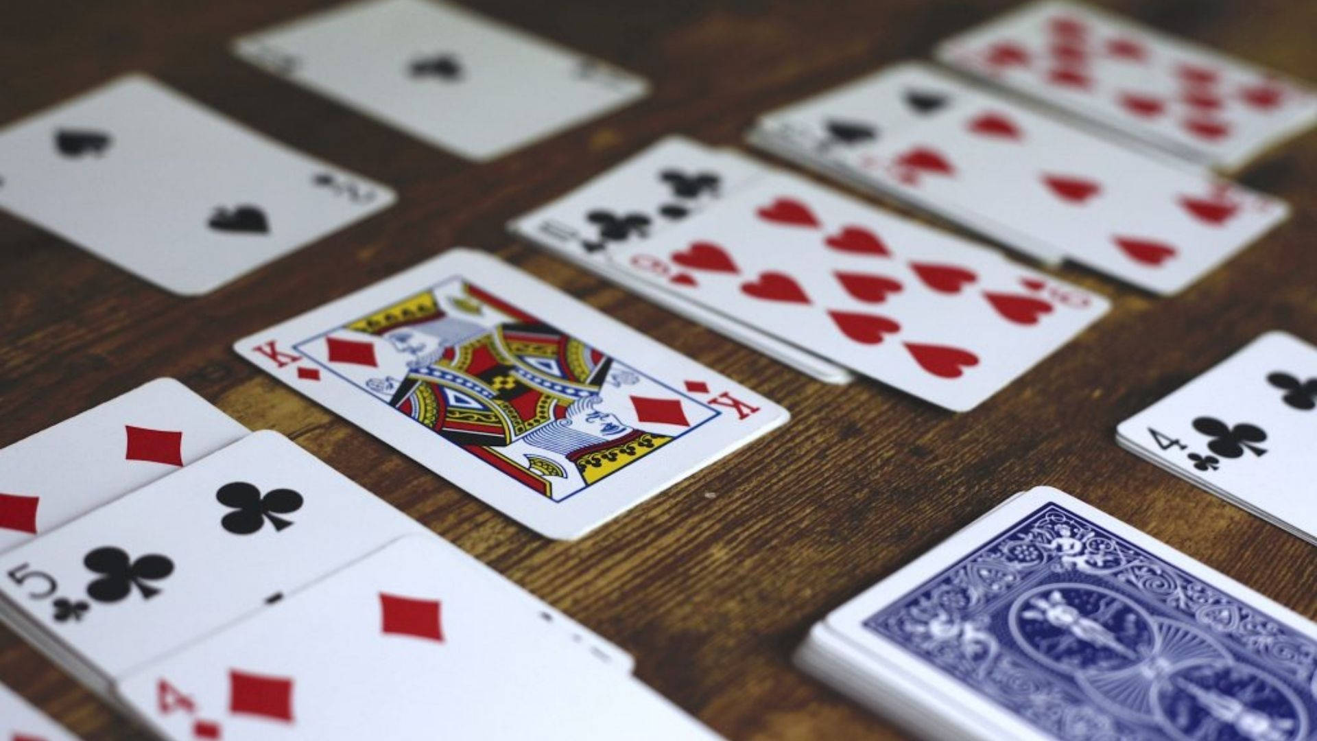 Solitaire 桌布 壁紙 — 特寫鏡頭：散落的撲克牌在鄉村風格木桌上，搭配溫暖燈光。
