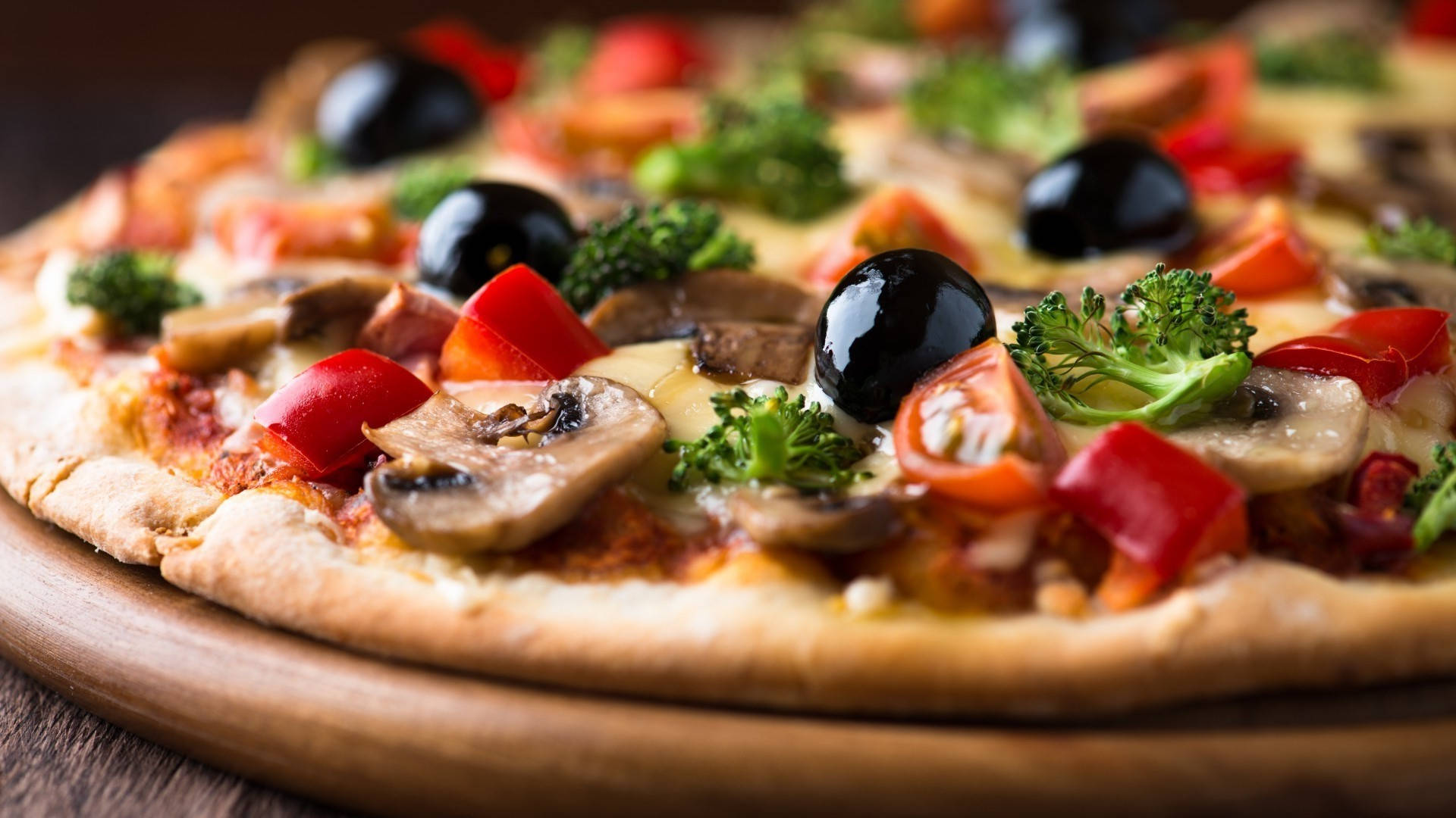 Pizza 桌布 壁紙 — 特寫鏡頭：新鮮出爐的披薩，上面有蘑菇、番茄、橄欖和花椰菜，放在木板上。