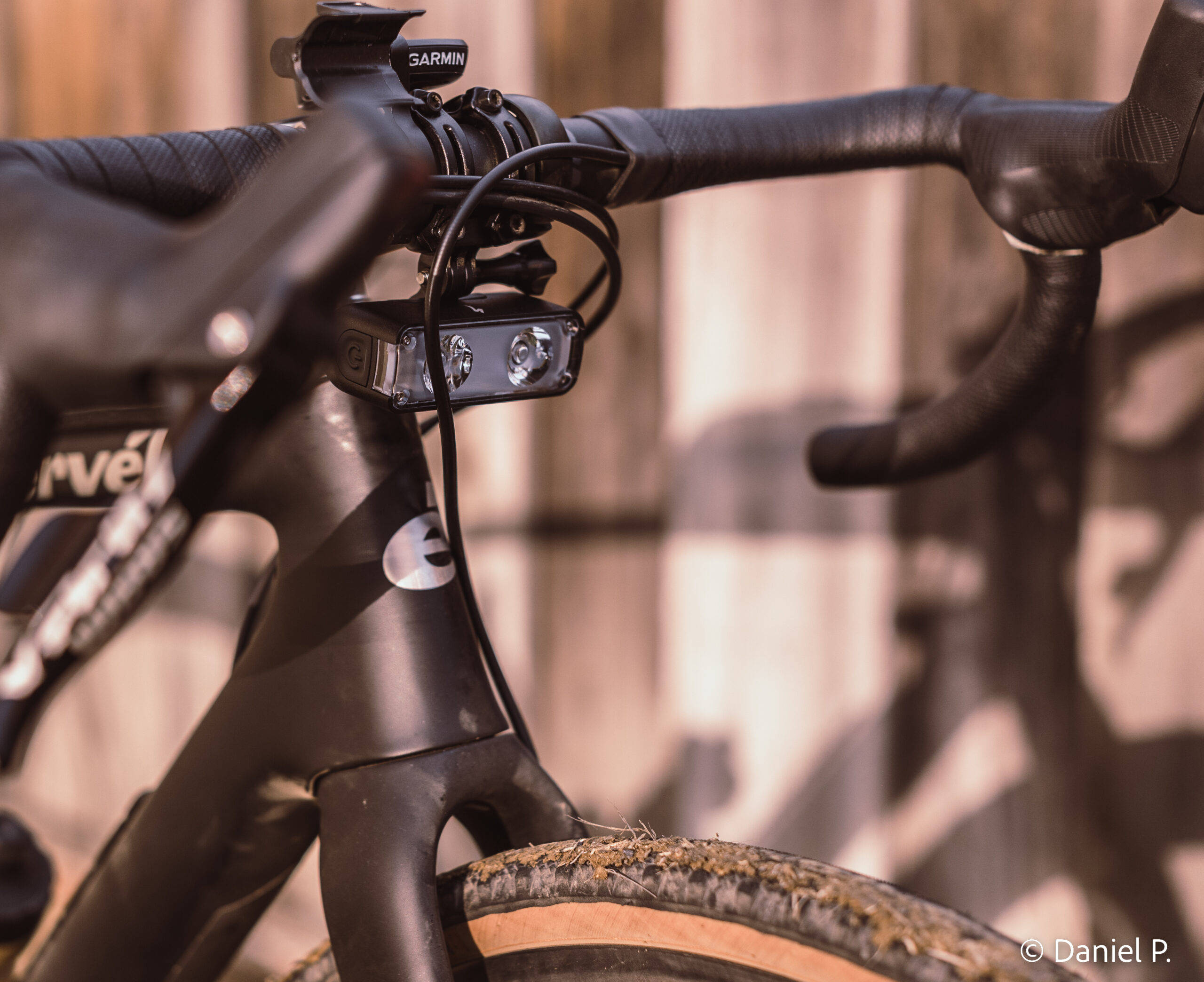 桌布 壁紙 — 特寫鏡頭：時尚黑色自行車把手，配備 Garmin 碼錶及前燈，背景為模糊的木柵欄。