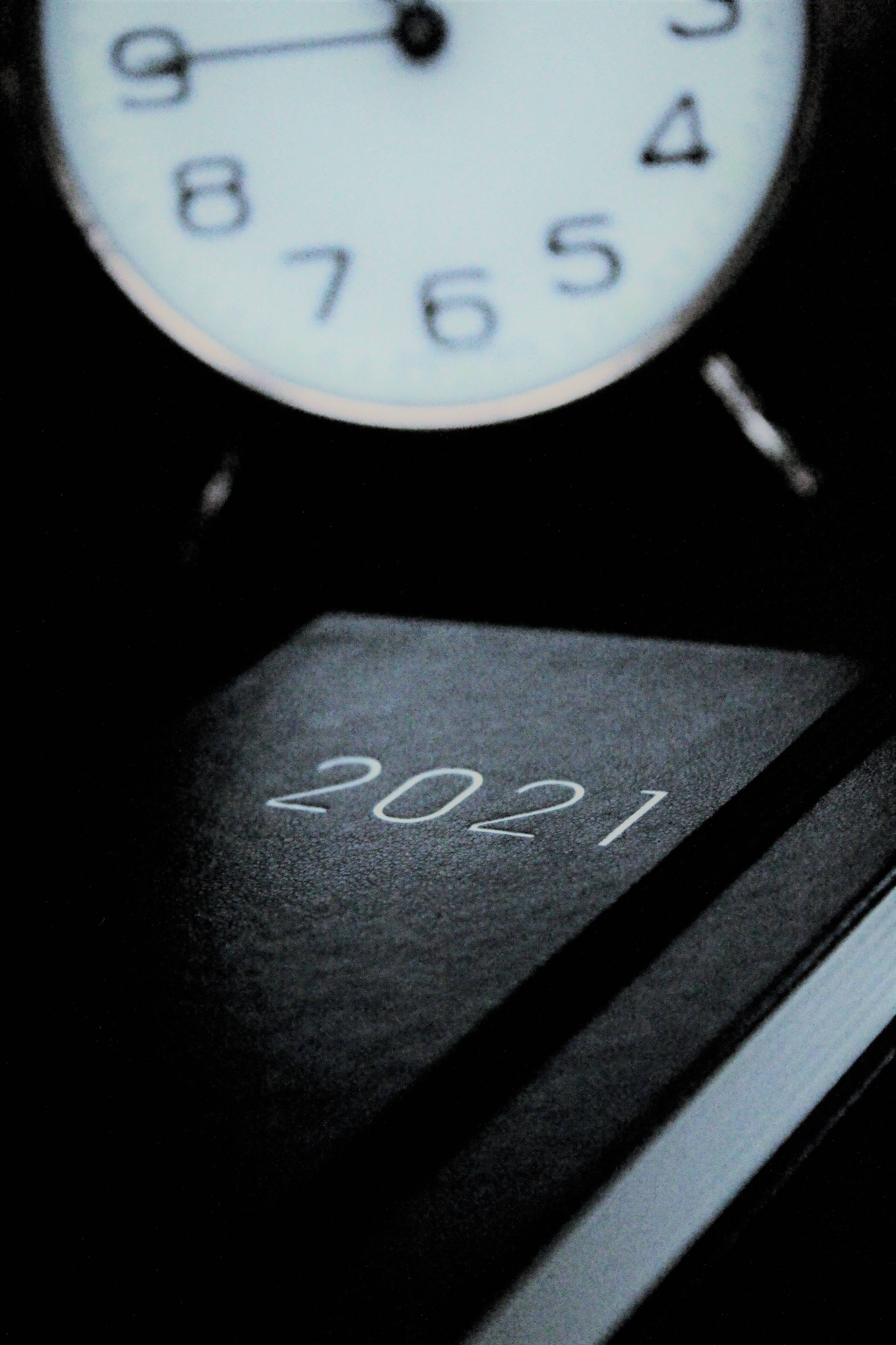 時鐘 桌布 壁紙 — 特寫鏡頭：時鐘置於2021年日曆書上方，昏暗燈光強調時間流逝。