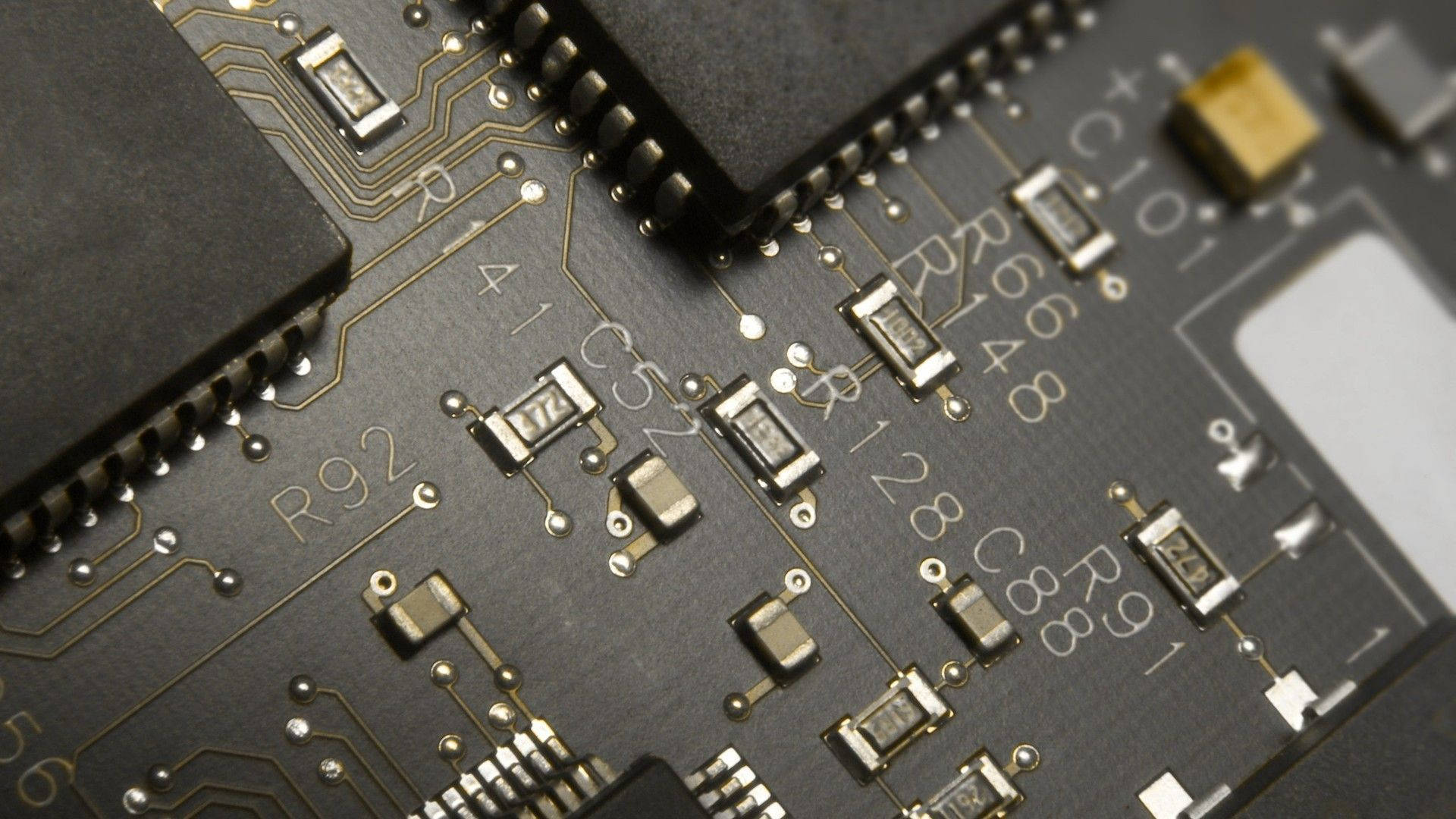 Circuit 桌布 壁紙 — 特寫鏡頭：深灰色電路板，帶有金色線路和微小電子元件，在明亮燈光下。