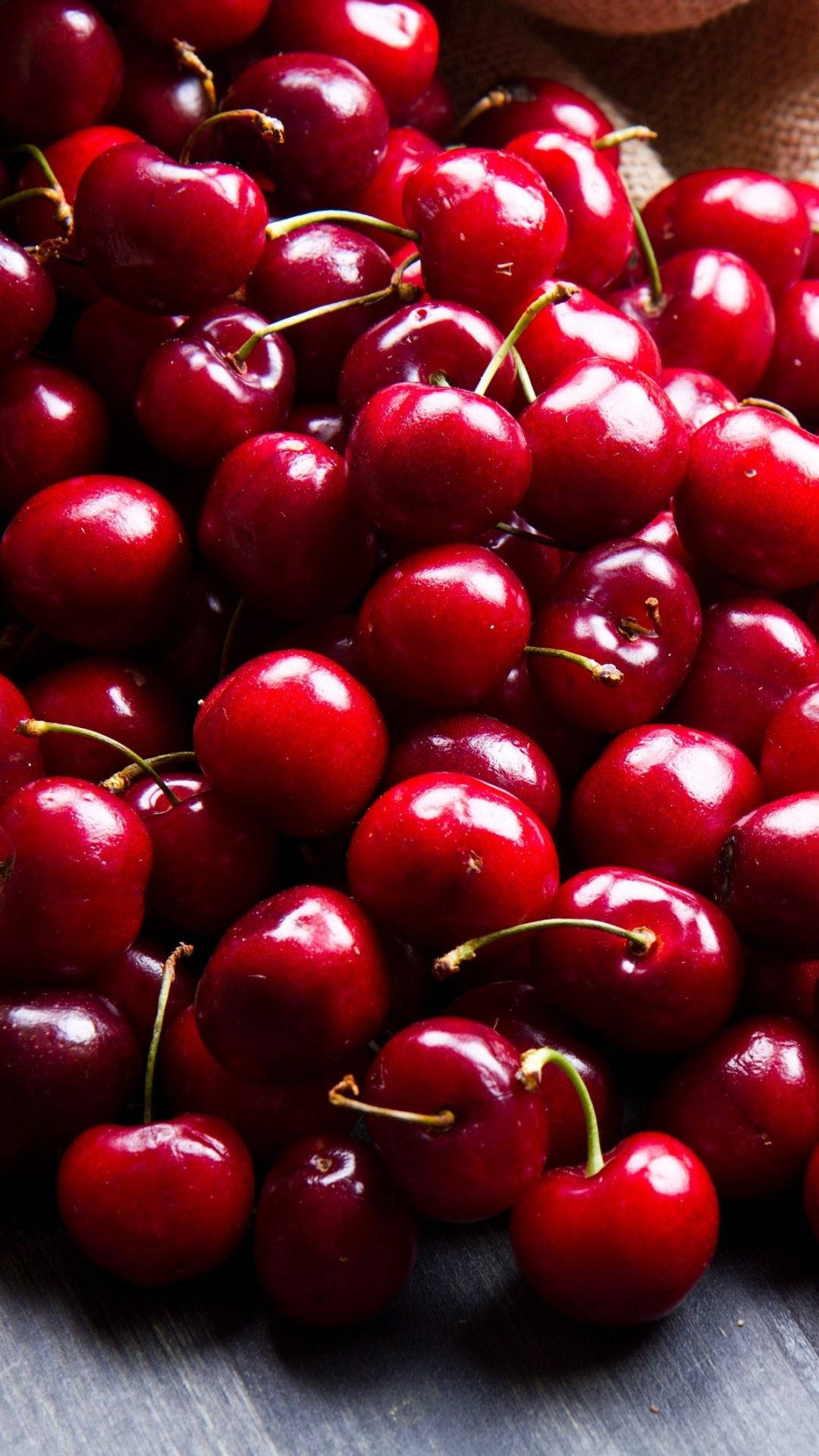 Fruit 桌布 壁紙 — 特寫鏡頭：深紅色光澤櫻桃高高堆起，帶綠色莖，置於深色木質表面上。