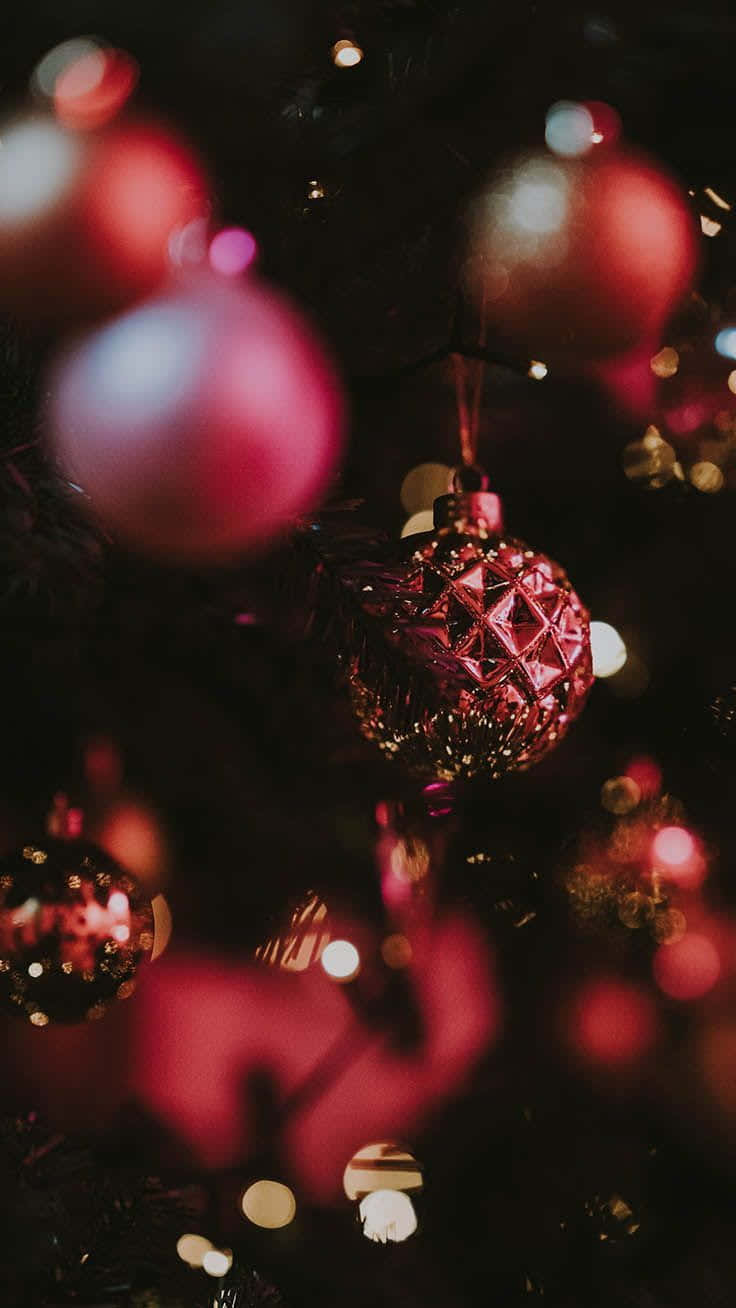 Red Aesthetic Christmas 桌布 壁紙 — 特寫鏡頭：深色聖誕樹上閃爍的紅色和粉紅色裝飾品，伴隨著柔和發光的散景燈光。