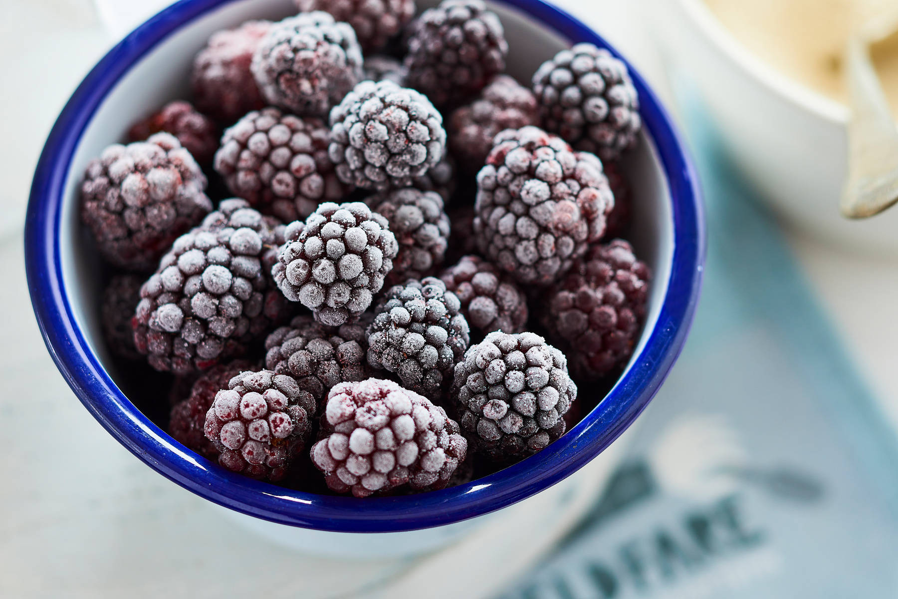 Berry 桌布 壁紙 — 特寫鏡頭：淺色表面上一個藍邊白碗內結霜的黑莓。