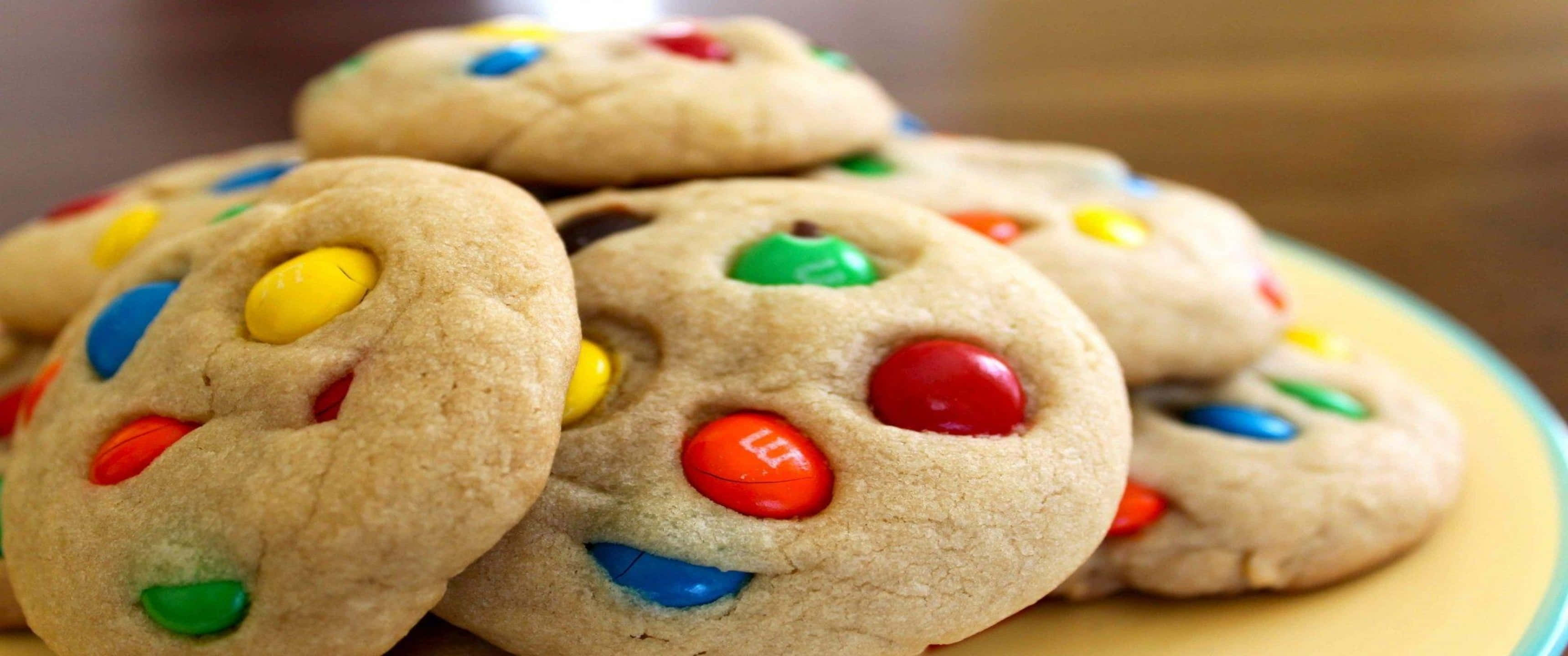 Cookies 桌布 壁紙 — 特寫鏡頭：溫暖金黃色的餅乾上綴滿色彩繽紛的M&M糖果，誘人地堆疊在盤子上。