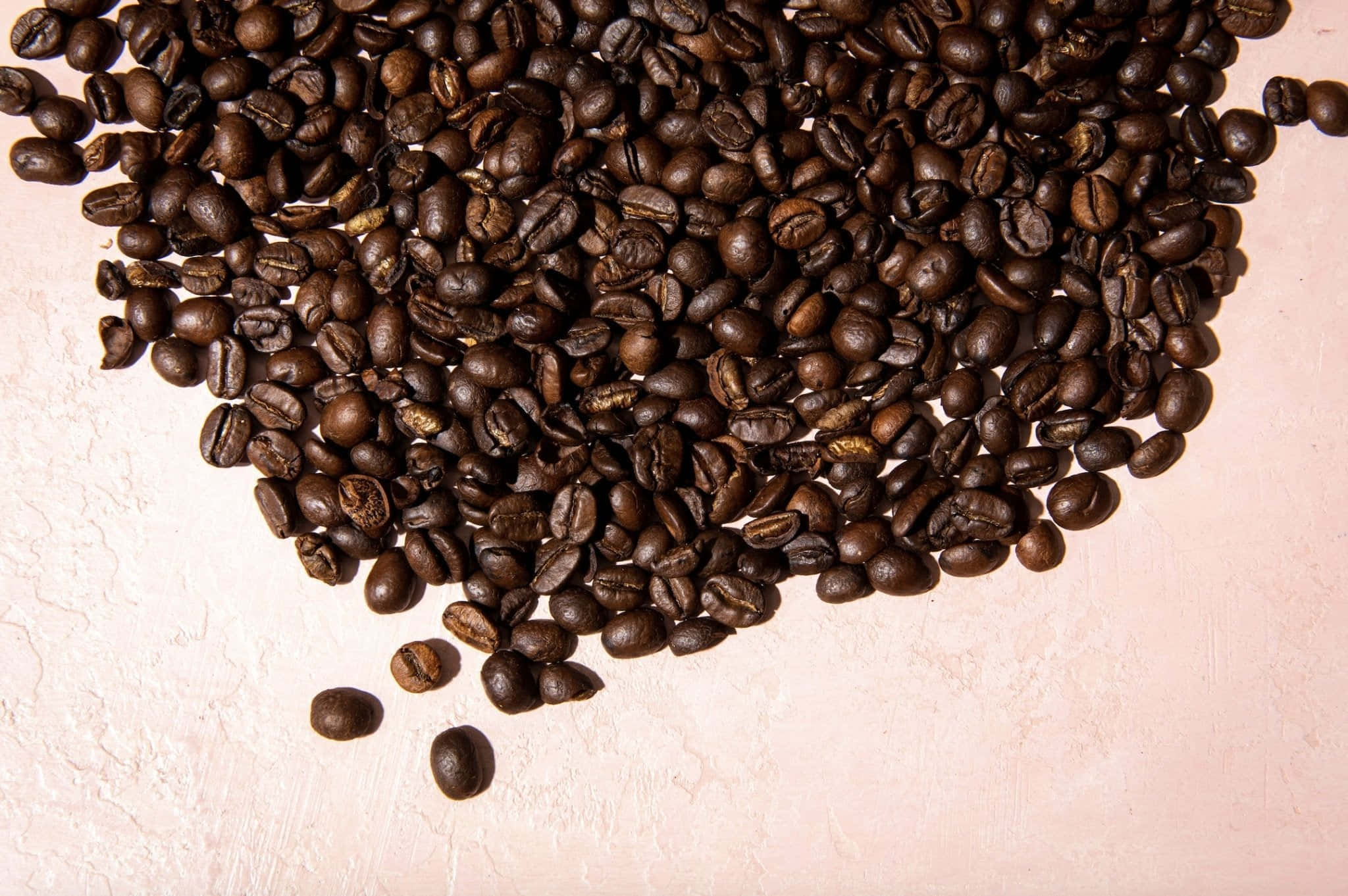 Coffee Beans 桌布 壁紙 — 特寫鏡頭：烘焙咖啡豆在帶有紋理的淡粉色表面上散落成心形。