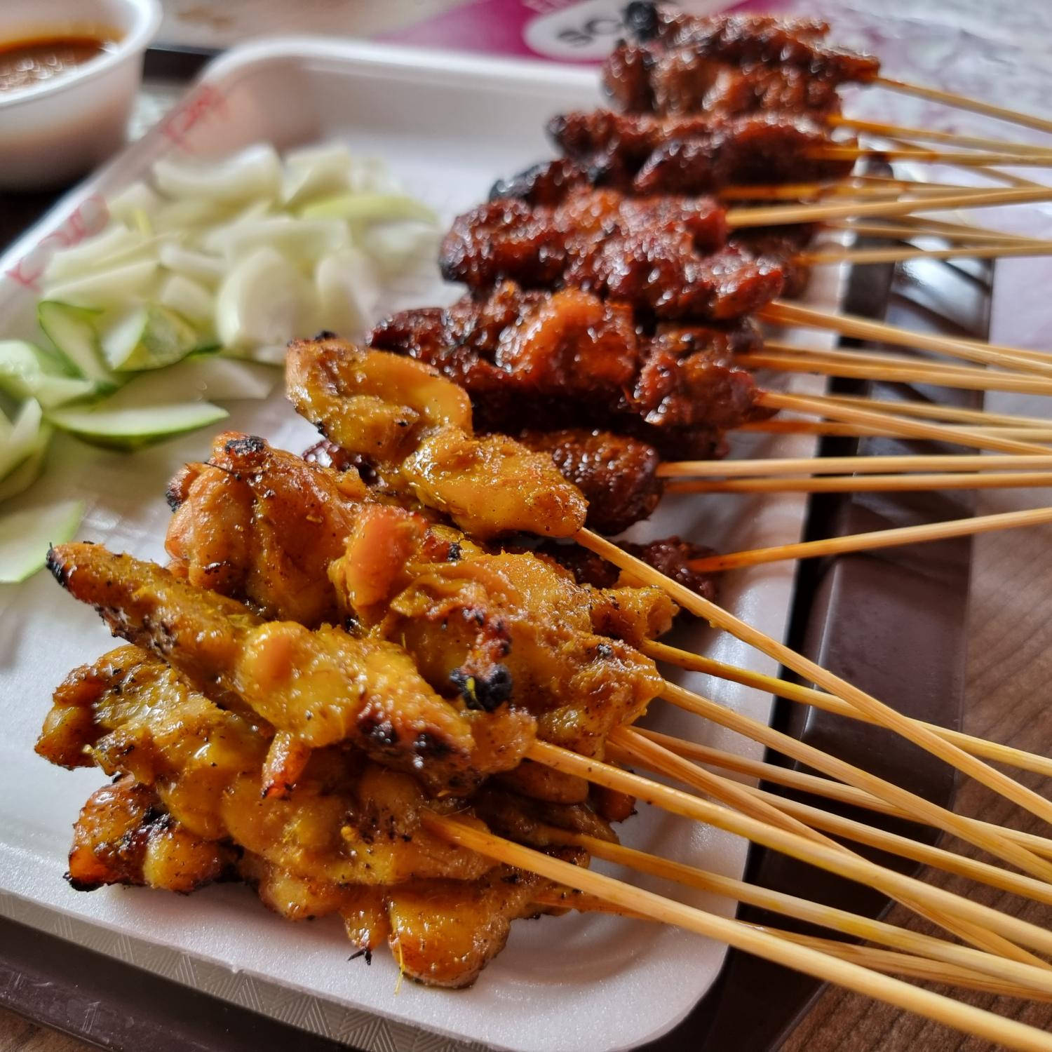 Satay 桌布 壁紙 — 特寫鏡頭：烤雞肉沙爹串，配上切片小黃瓜和洋蔥，放在白色托盤上。