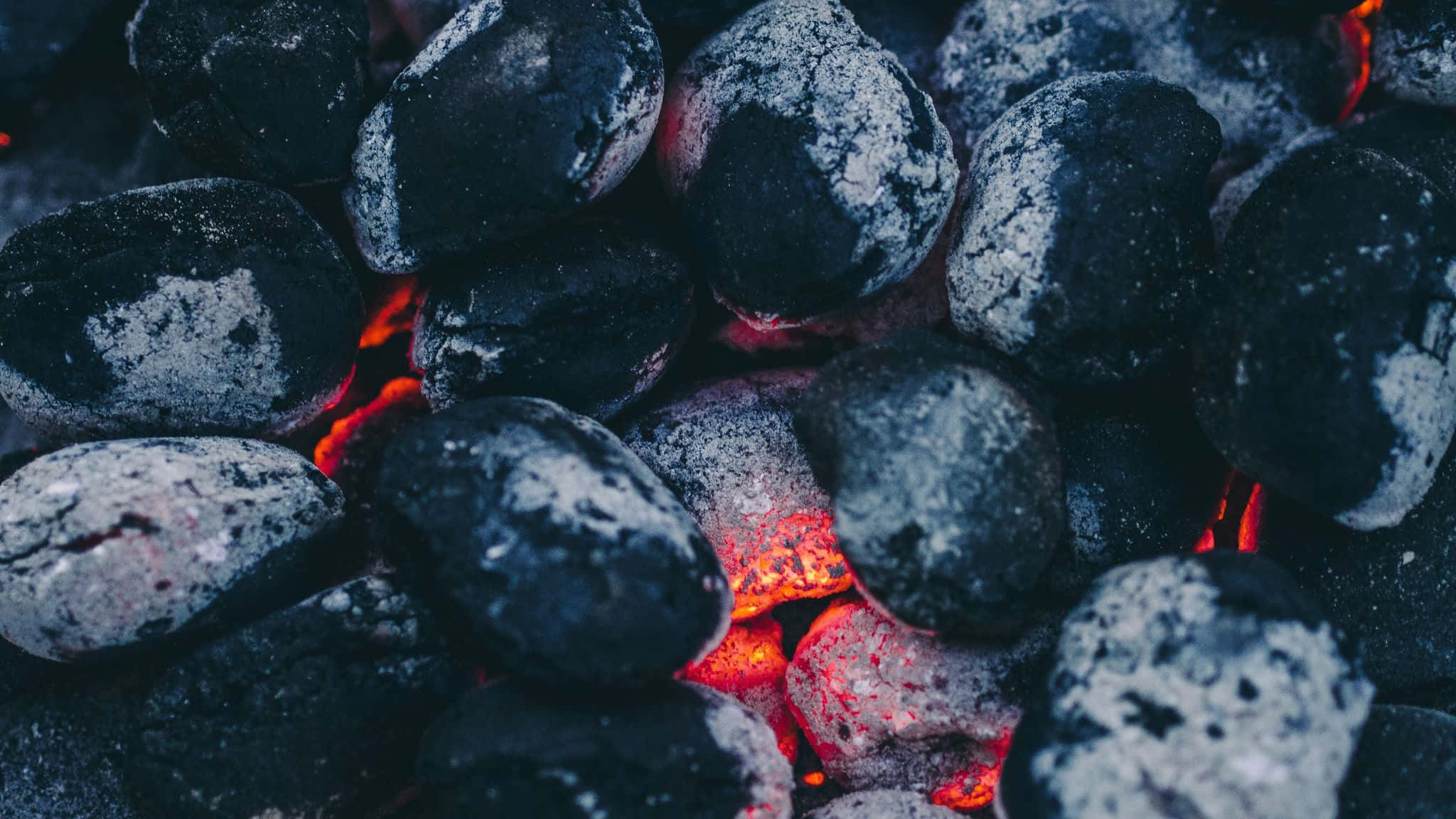Charcoal 桌布 壁紙 — 特寫鏡頭：發光的餘燼依偎在深色灰燼覆蓋的木炭碎片之間，散發溫暖。