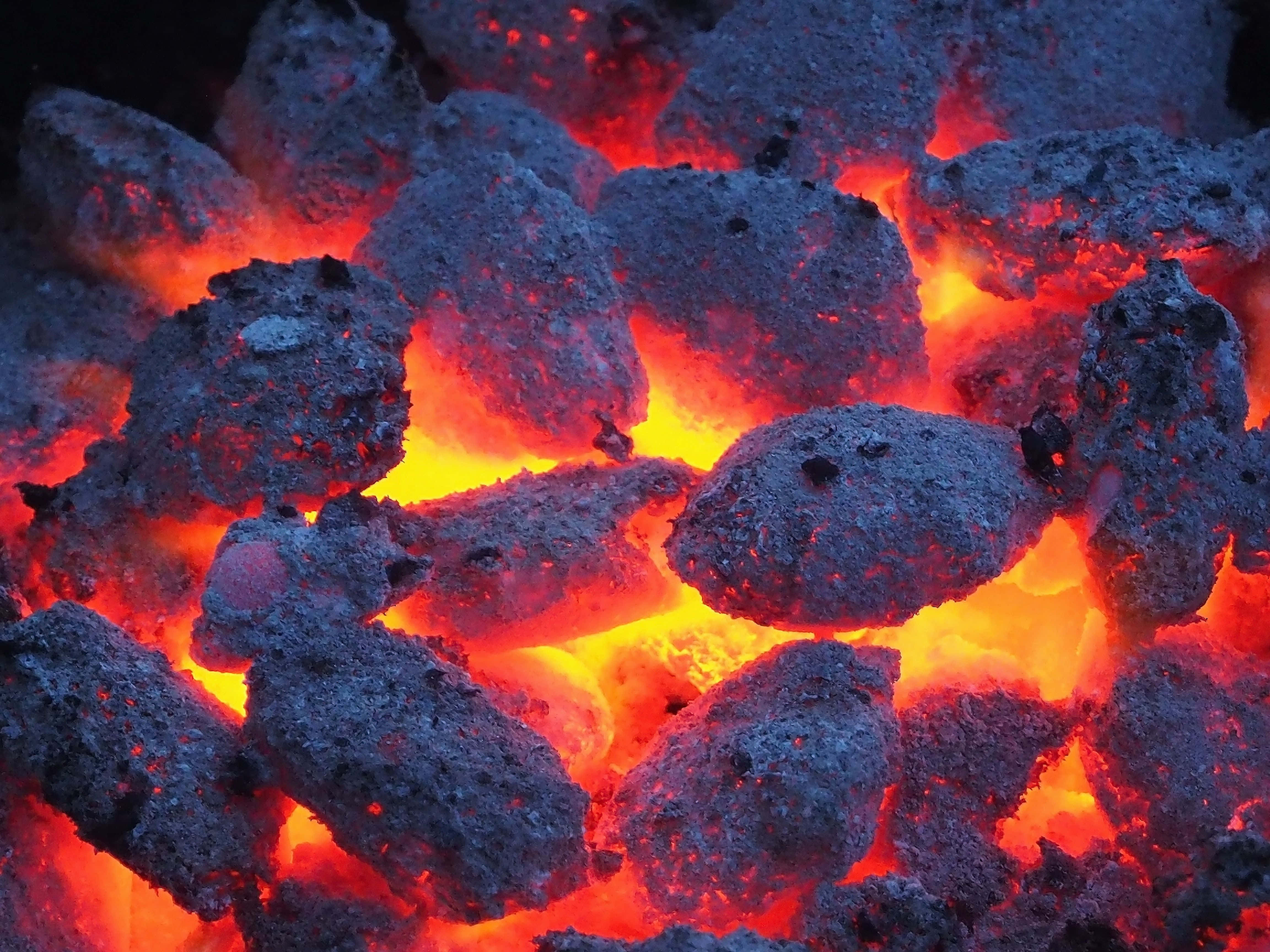Charcoal 桌布 壁紙 — 特寫鏡頭，發光的餘燼在深色木炭碎片襯托下散發出強烈的橙色和紅色熱量。
