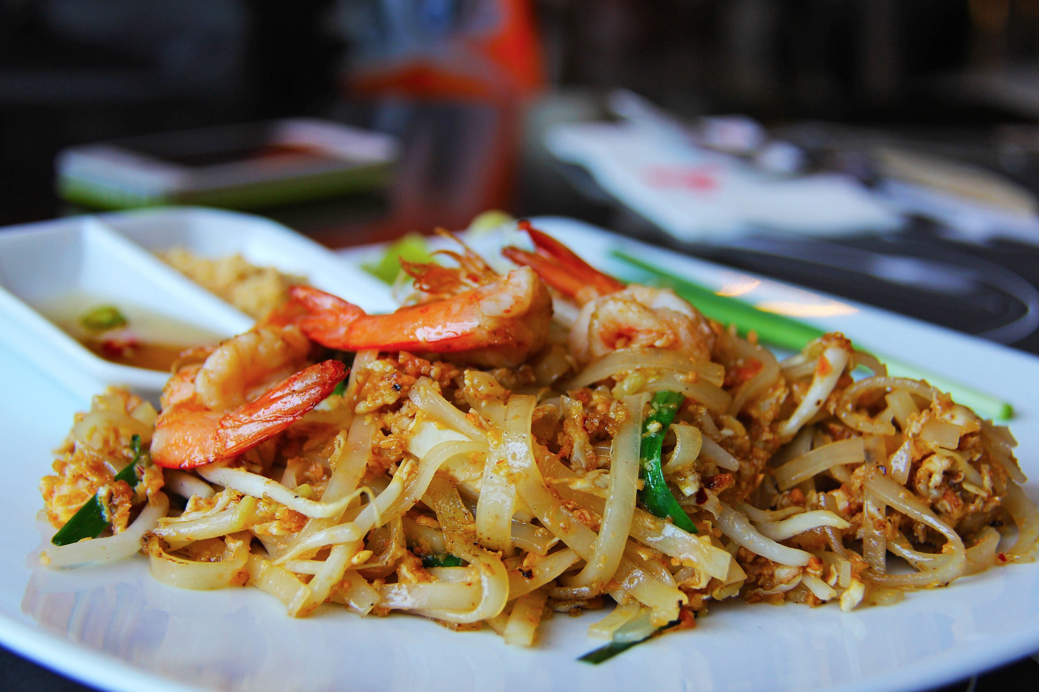 thai 桌布 壁紙 — 特寫鏡頭：白盤上冒著熱氣的泰式炒河粉，配蝦仁、青蔥和花生。