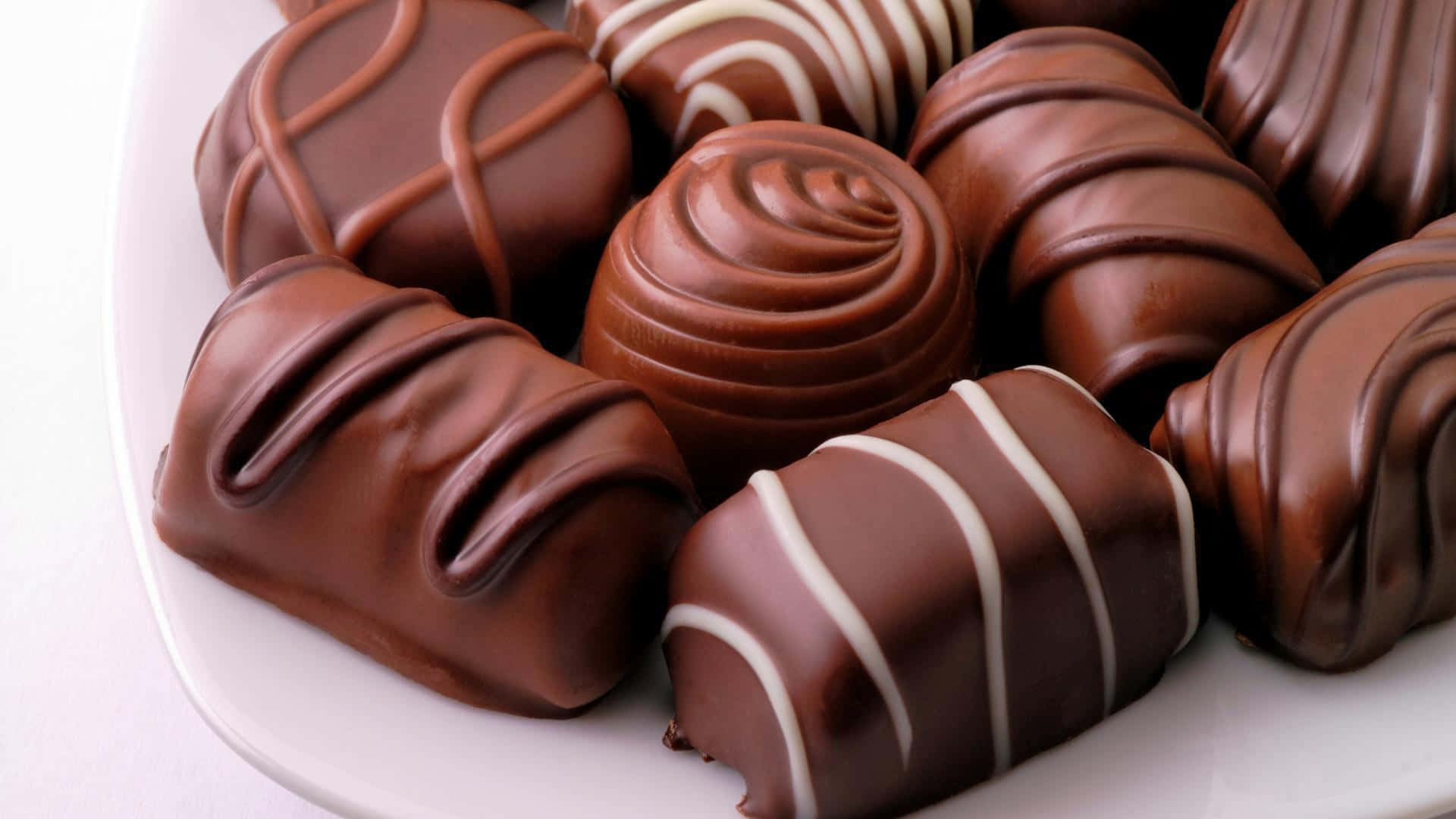Brown Chocolate 桌布 壁紙 — 特寫鏡頭：白色盤子上各種光澤巧克力糖果，帶有白色淋醬。