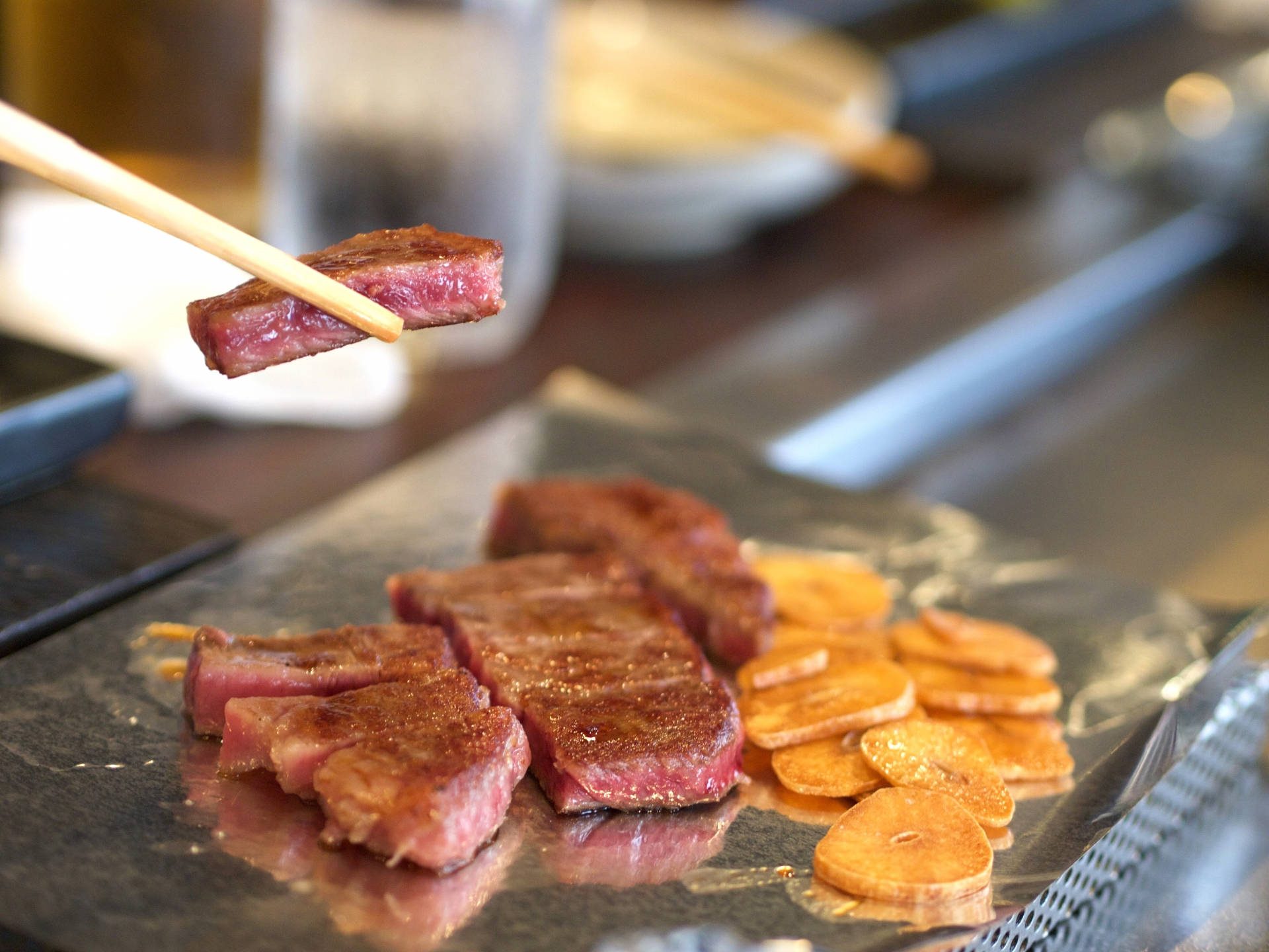 meat 桌布 壁紙 — 特寫鏡頭：筷子夾起完美煎烤的牛肉片，置於熱烤盤上，旁邊伴以金黃薯片。