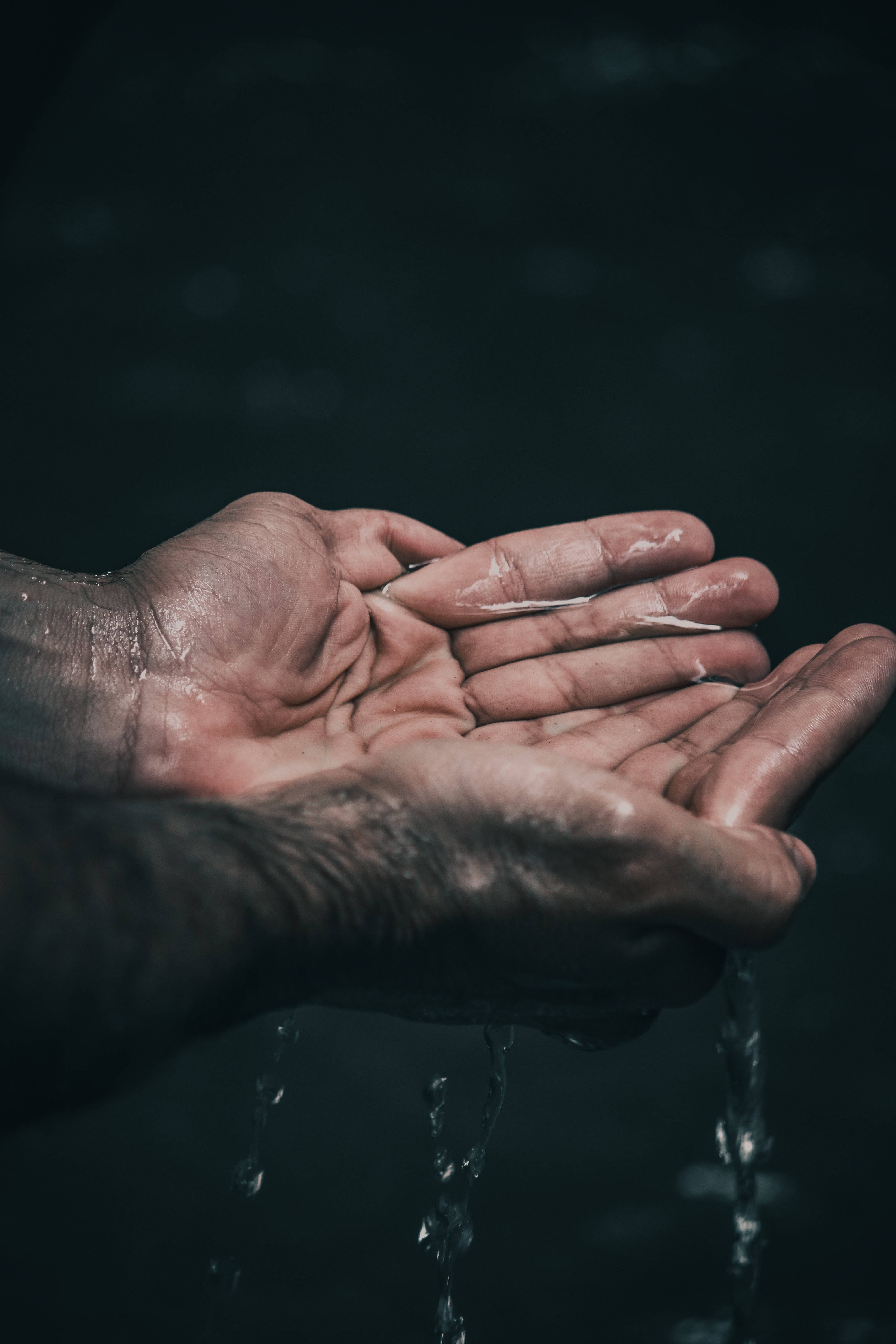 水 桌布 壁紙 — 特寫鏡頭：粗糙的雙手捧起並釋放清澈的水，背景為黑暗模糊。