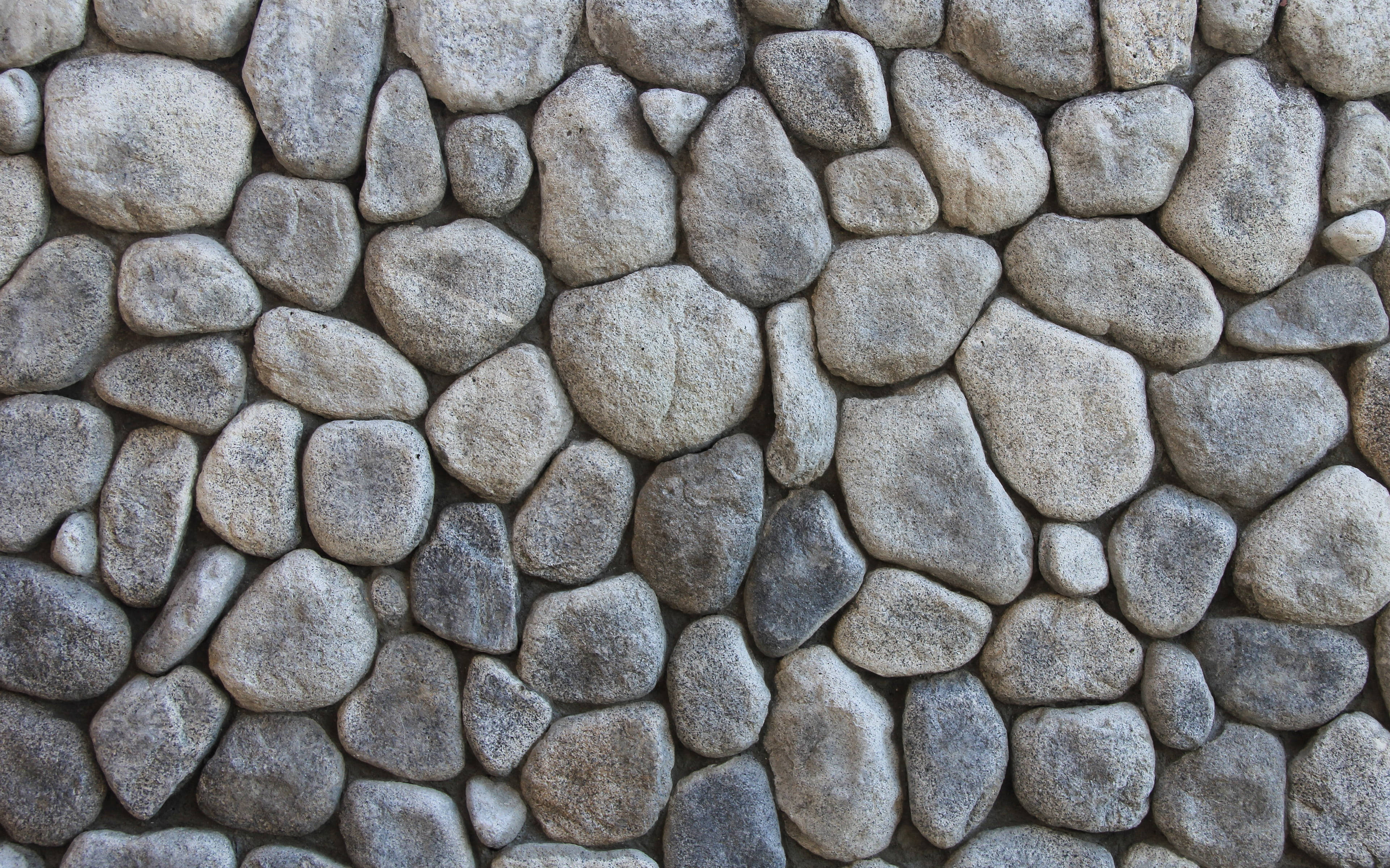 Stone Wall 桌布 壁紙 — 特寫鏡頭：紋理石牆，由不規則形狀的灰色和米色岩石緊密嵌合而成。