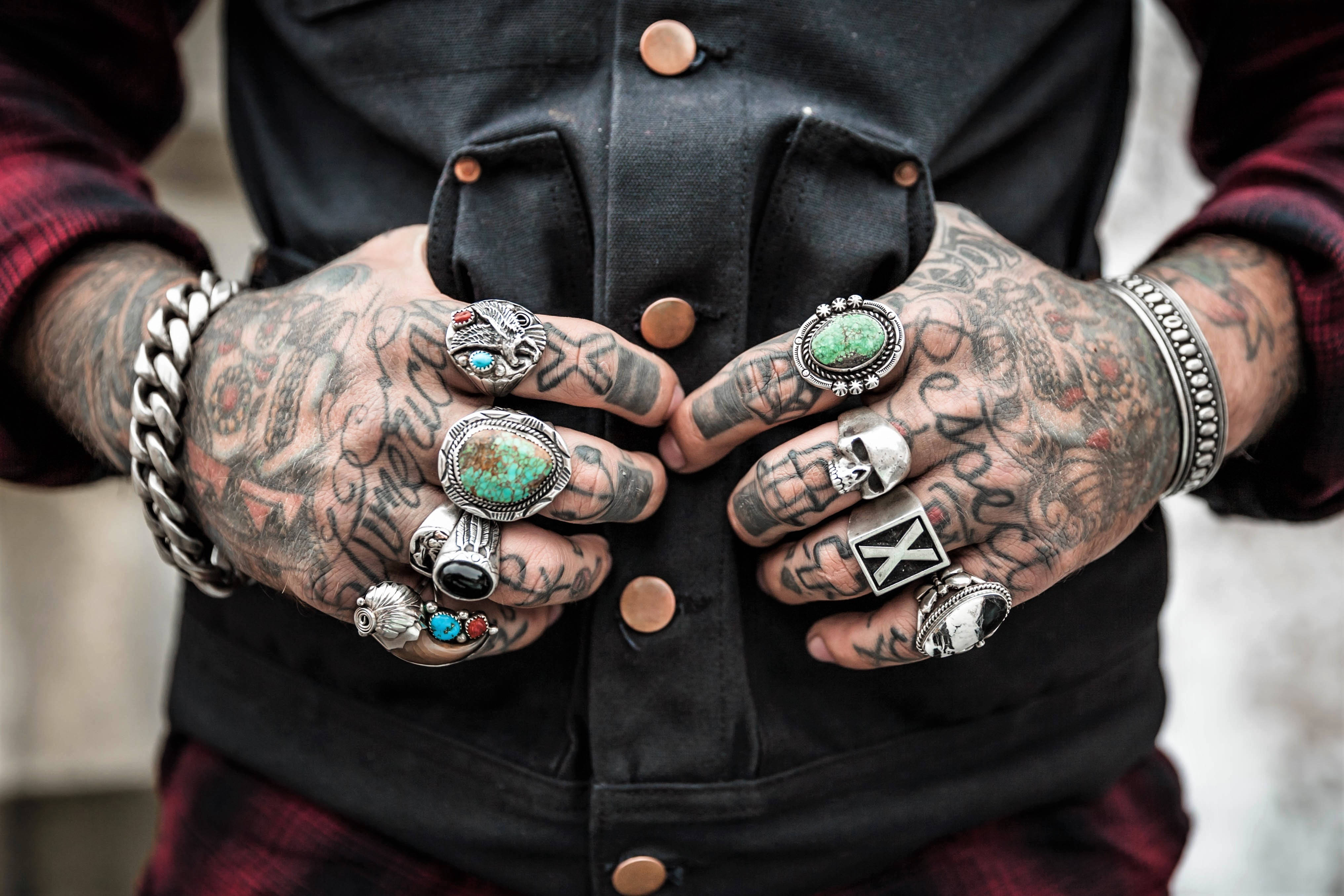 Tattoo 桌布 壁紙 — 特寫鏡頭：紋身雙手戴著多個華麗戒指和粗手鐲，襯托深色背心。