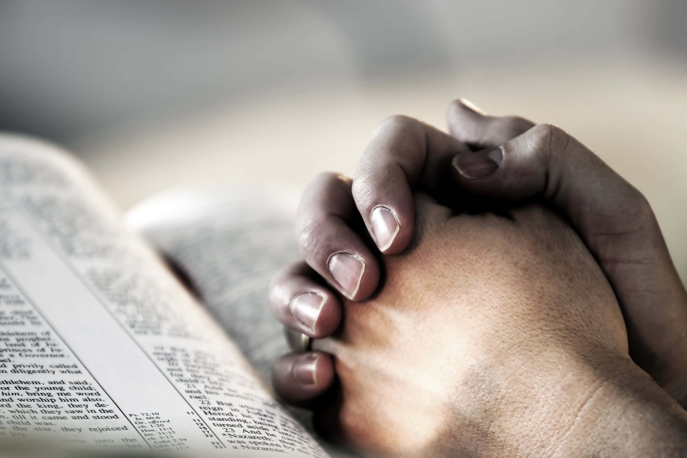 Praying 桌布 壁紙 — 特寫鏡頭：緊握的雙手放在打開的聖經上，柔和自然光突顯皮膚和書頁的質感。