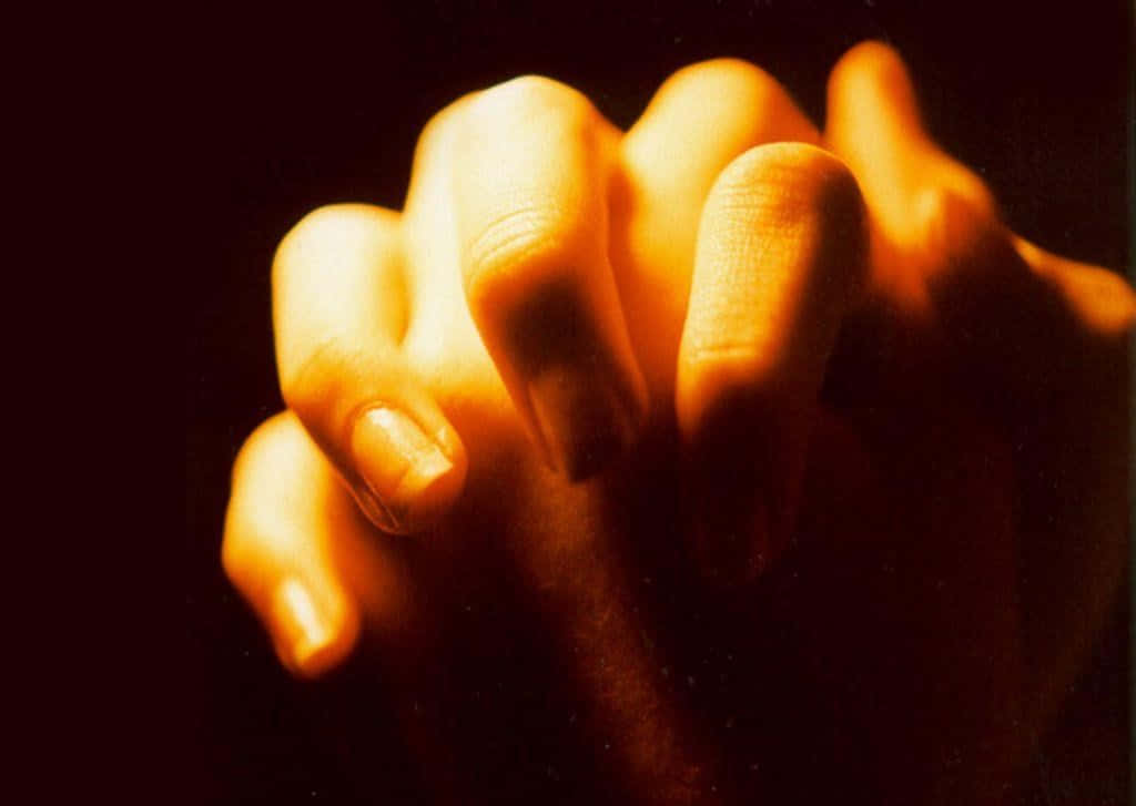 Praying 桌布 壁紙 — 特寫鏡頭，緊握的雙手沐浴在溫暖的金色光芒中，背景為深色。