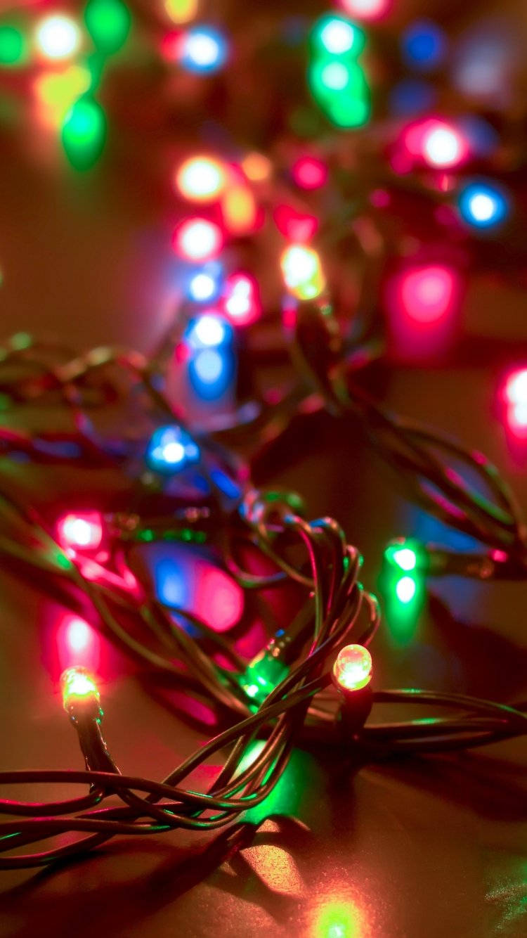 Christmas Lights Aesthetic 桌布 壁紙 — 特寫鏡頭，纏繞的彩色燈串在黑暗背景下發出溫暖的光芒，帶有紅色、綠色和藍色燈泡。