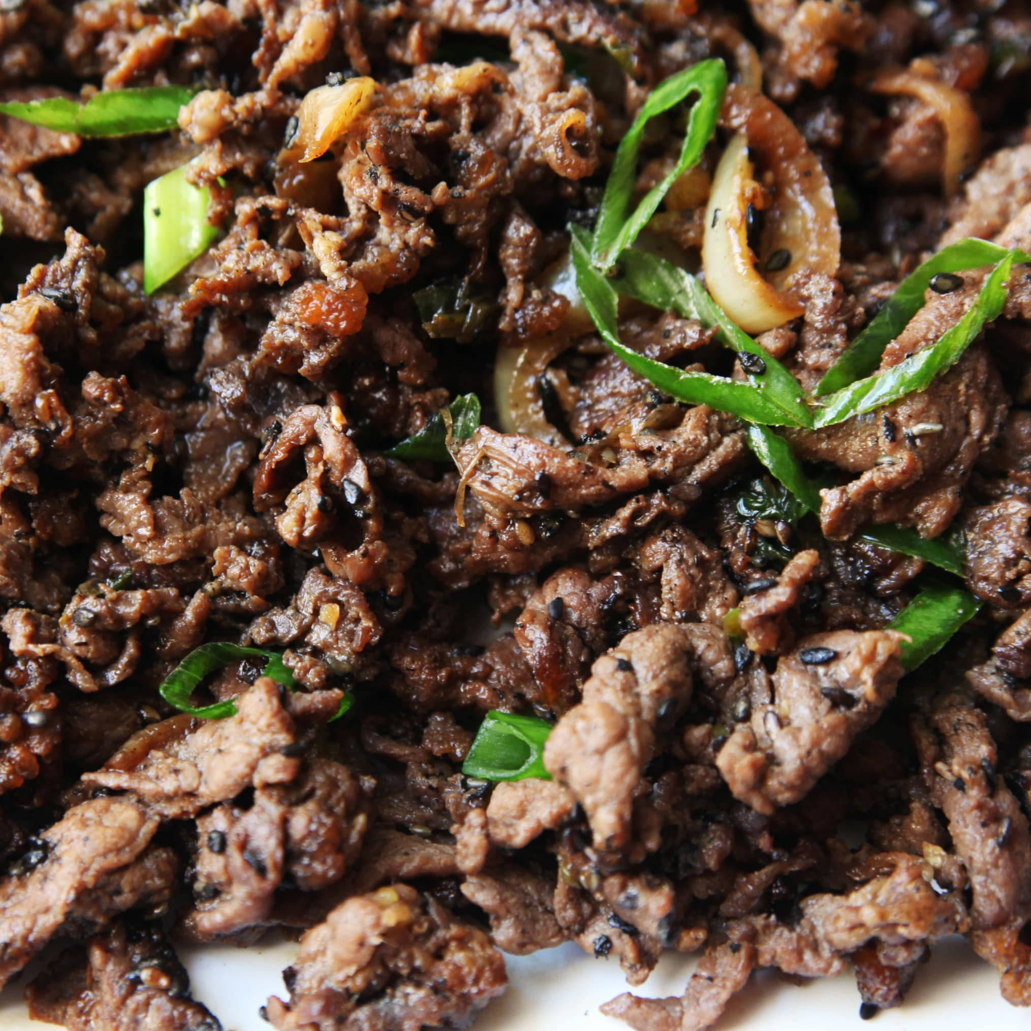 黑色 桌布 壁紙 — 特寫鏡頭：美味的炒牛肉條，搭配青蔥、芝麻和焦糖洋蔥，醬汁閃閃發光。