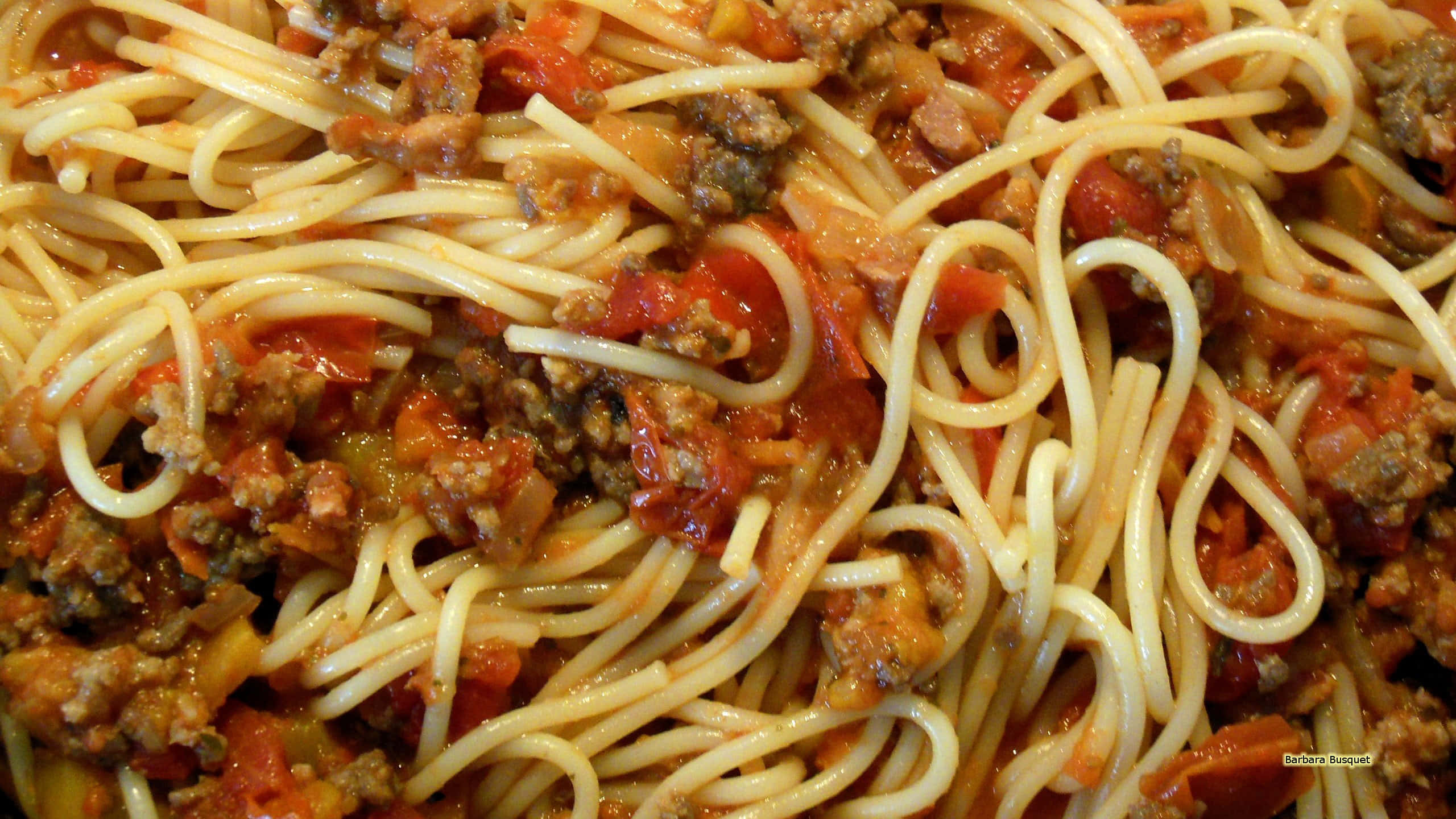 Pasta 桌布 壁紙 — 特寫鏡頭：義大利麵配上濃郁番茄醬和肉末，在溫暖燈光下閃閃發光。
