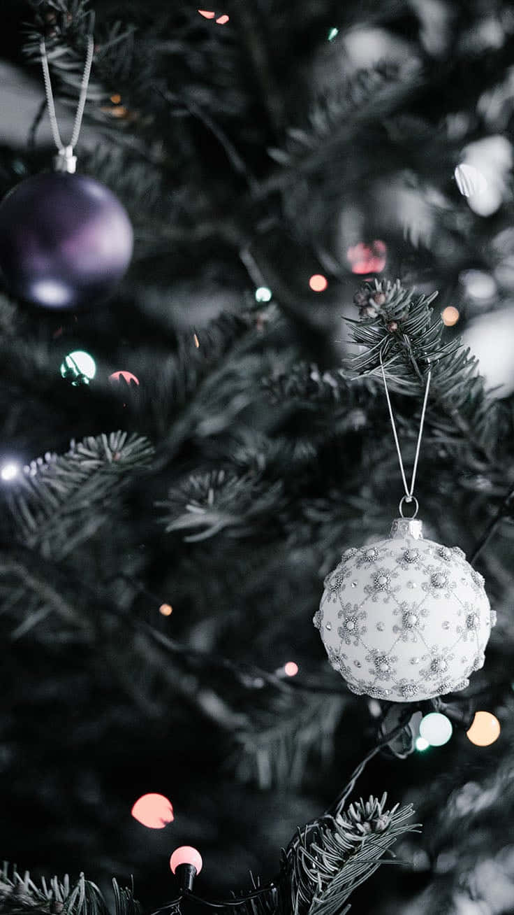White Christmas iPhone 桌布 壁紙 — 特寫鏡頭：裝飾好的聖誕樹，帶有白色華麗飾球和紫色裝飾，背景是模糊的節日燈光。