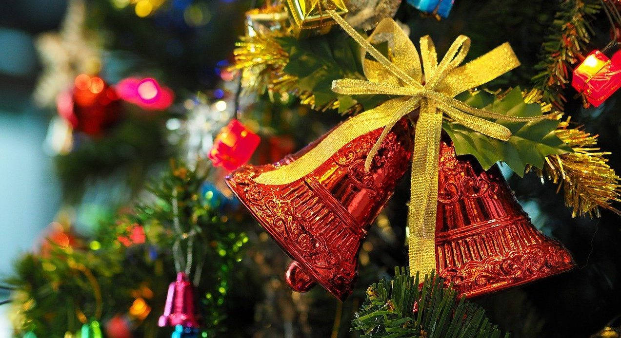 Christmas Bell 桌布 壁紙 — 特寫鏡頭：裝飾華麗的紅色鈴鐺用金色絲帶繫在裝飾著閃爍燈光的聖誕樹上。