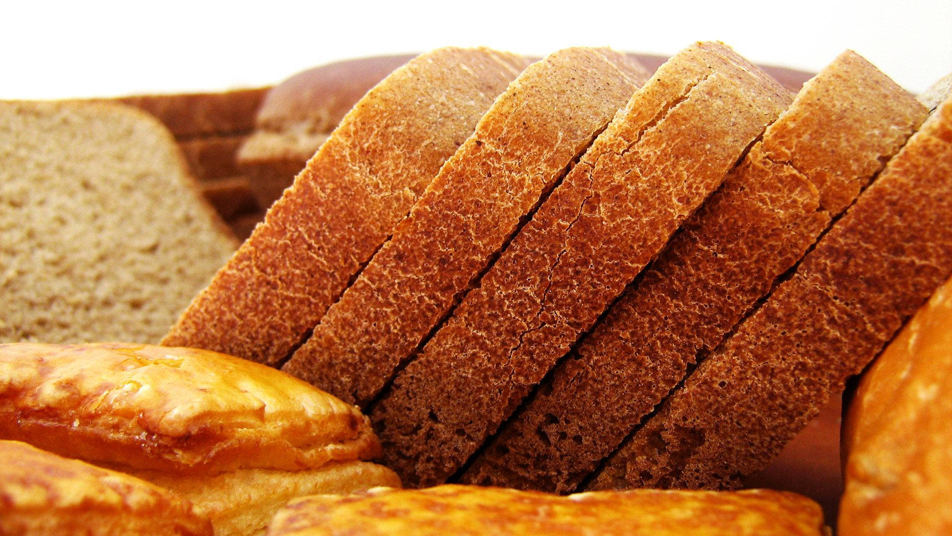 Bread 桌布 壁紙 — 特寫鏡頭：金黃色的全麥麵包切片，旁邊放著酥皮糕點，背景是明亮的白色。