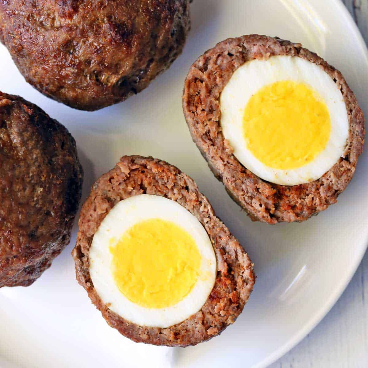 Egg 桌布 壁紙 — 特寫鏡頭：金黃蛋黃的水煮蛋鑲嵌在棕色肉餅半塊中，置於白色盤子上。