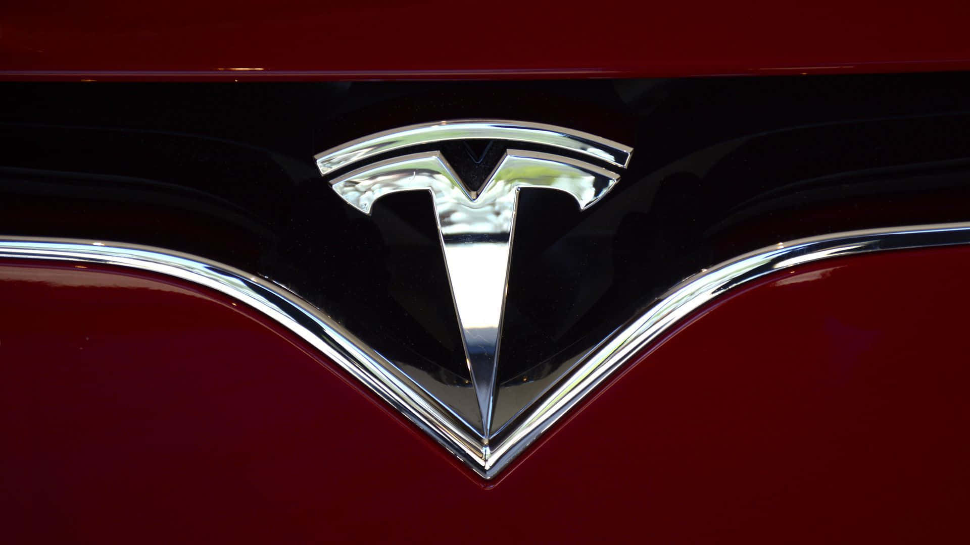 桌布 壁紙 — 特寫鏡頭：閃亮鍍鉻 Tesla 標誌置於帶黑色飾邊的亮紅色引擎蓋中央。