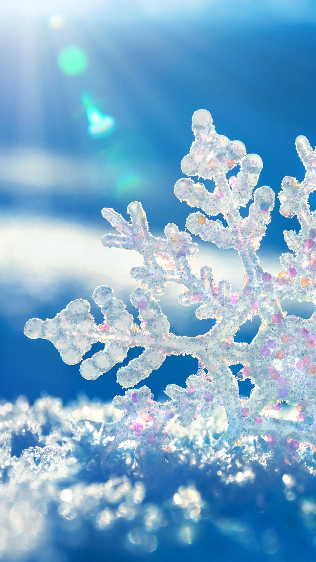 雪花 桌布 壁紙 — 特寫鏡頭：閃閃發光的雪花，帶有虹彩粉紅色和紫色亮點，背景是明亮的藍天和鏡頭光暈。