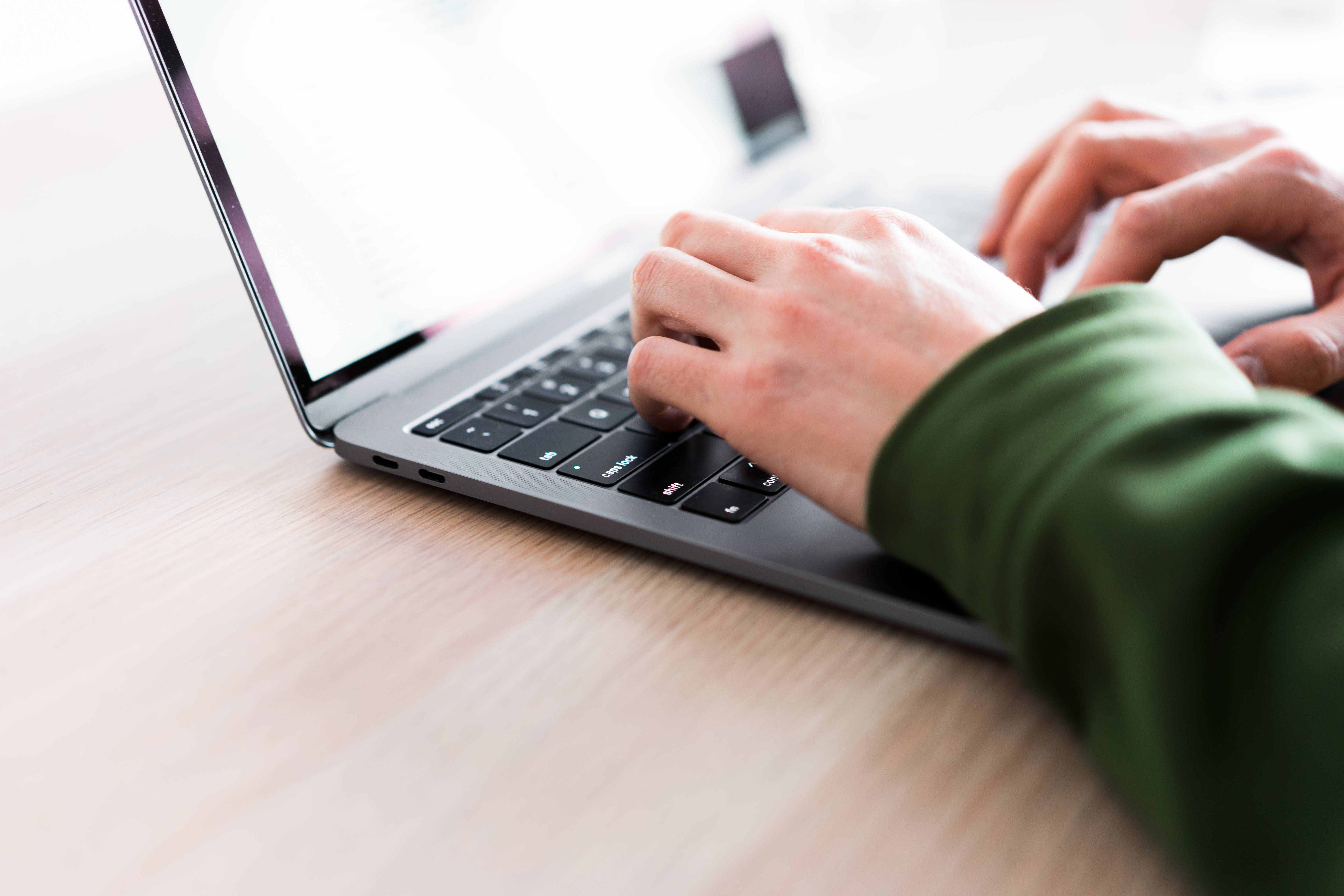typing 桌布 壁紙 — 特寫鏡頭：雙手在柔和的自然光下，於淺色木桌上輕巧的銀色筆記型電腦上打字。