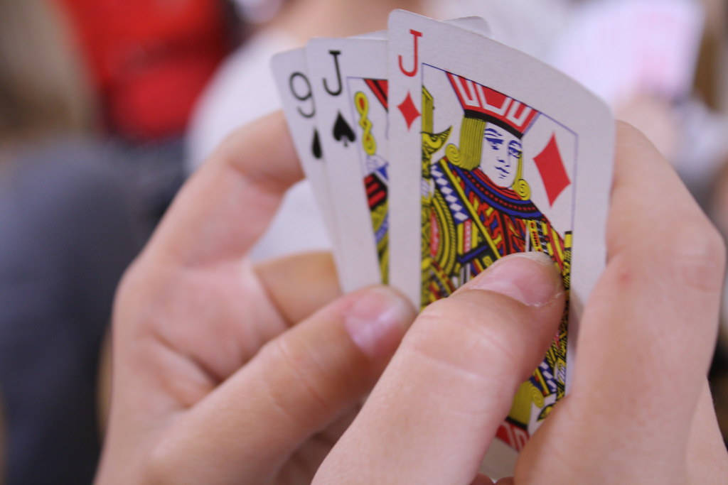Casino 桌布 壁紙 — 特寫鏡頭，雙手在模糊背景中拿著撲克牌的皇家同花順。